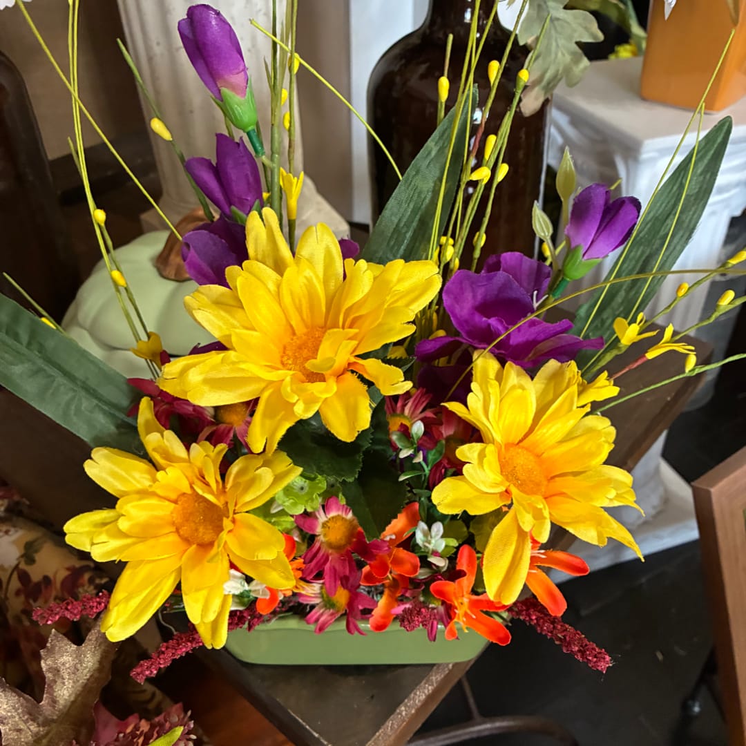 Bright yellow and purple floral arrangement in a green container