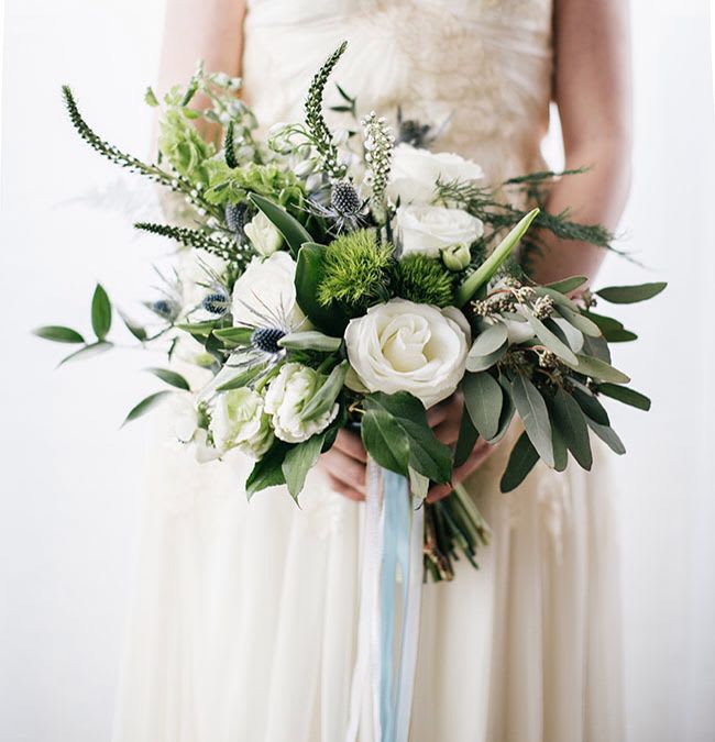 Bride holding a white and green bouquet with ribbon streamers