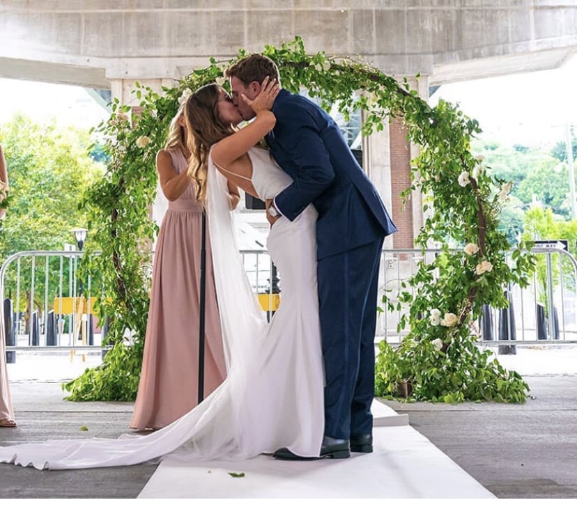 Bride and groom kissing under a greenery-covered wedding arch
