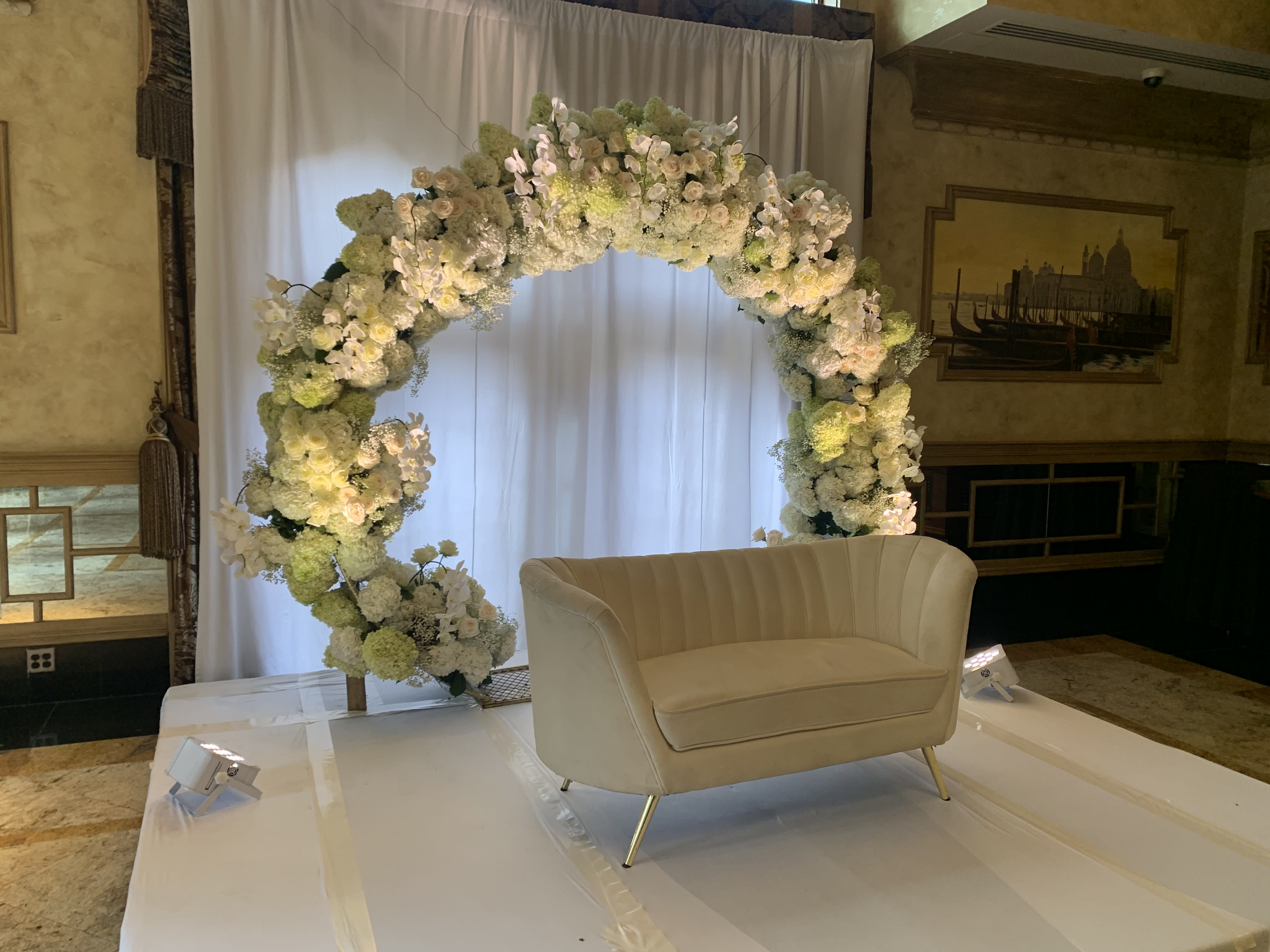 White floral arch behind a cream loveseat on a stage