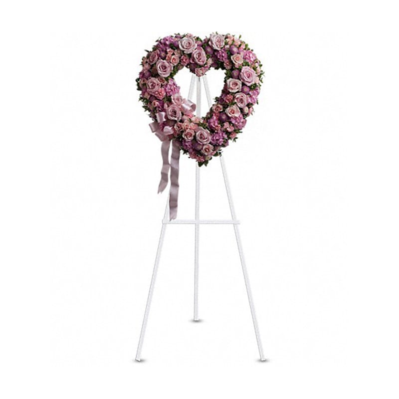 Heart-shaped pink rose wreath on a white stand with ribbon