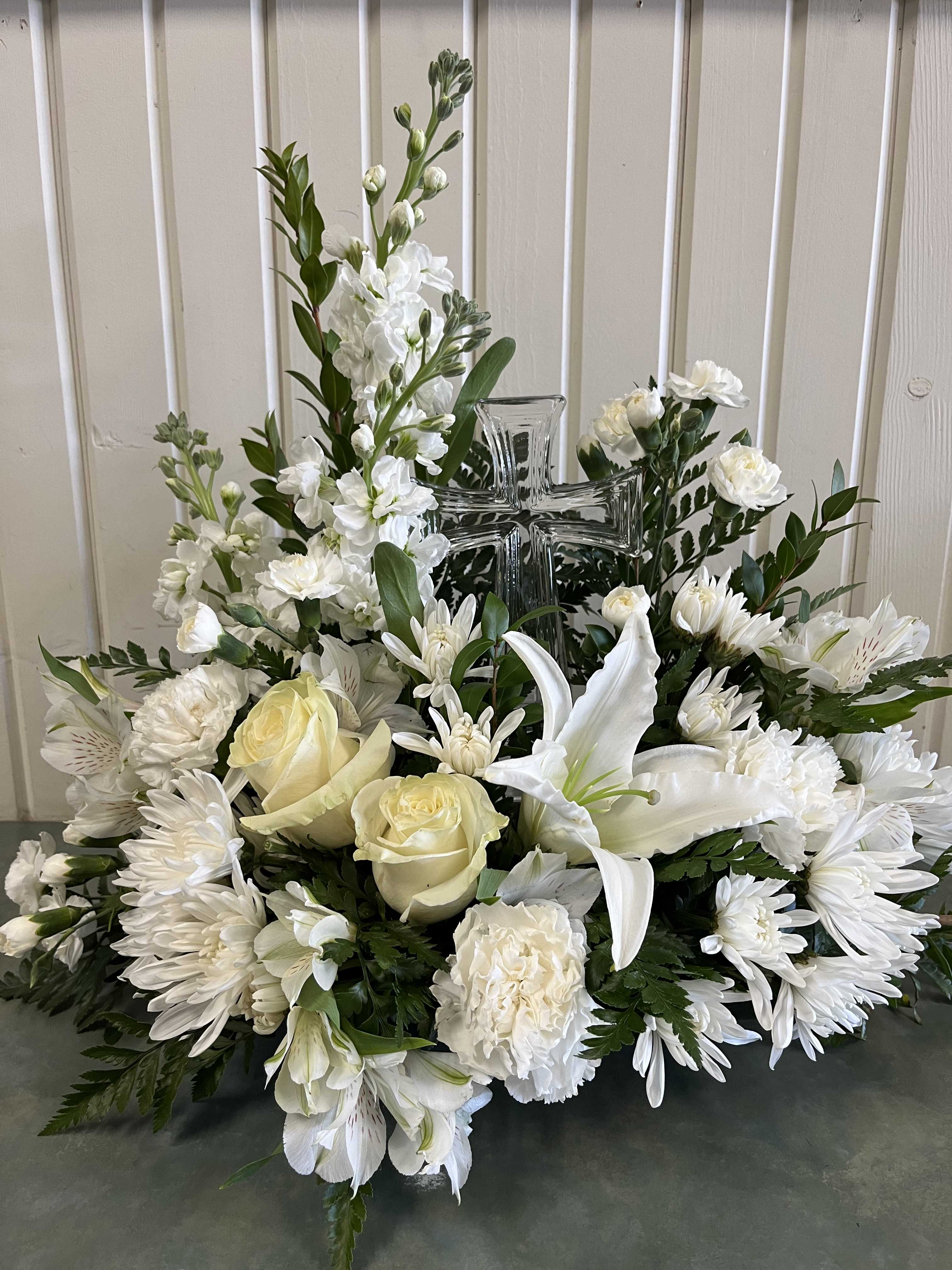 White floral arrangement with roses, lilies, and a glass cross