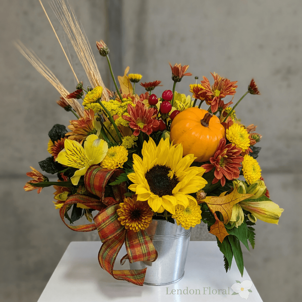 Fall floral arrangement with sunflowers, mums, and a small pumpkin in a metal bucket
