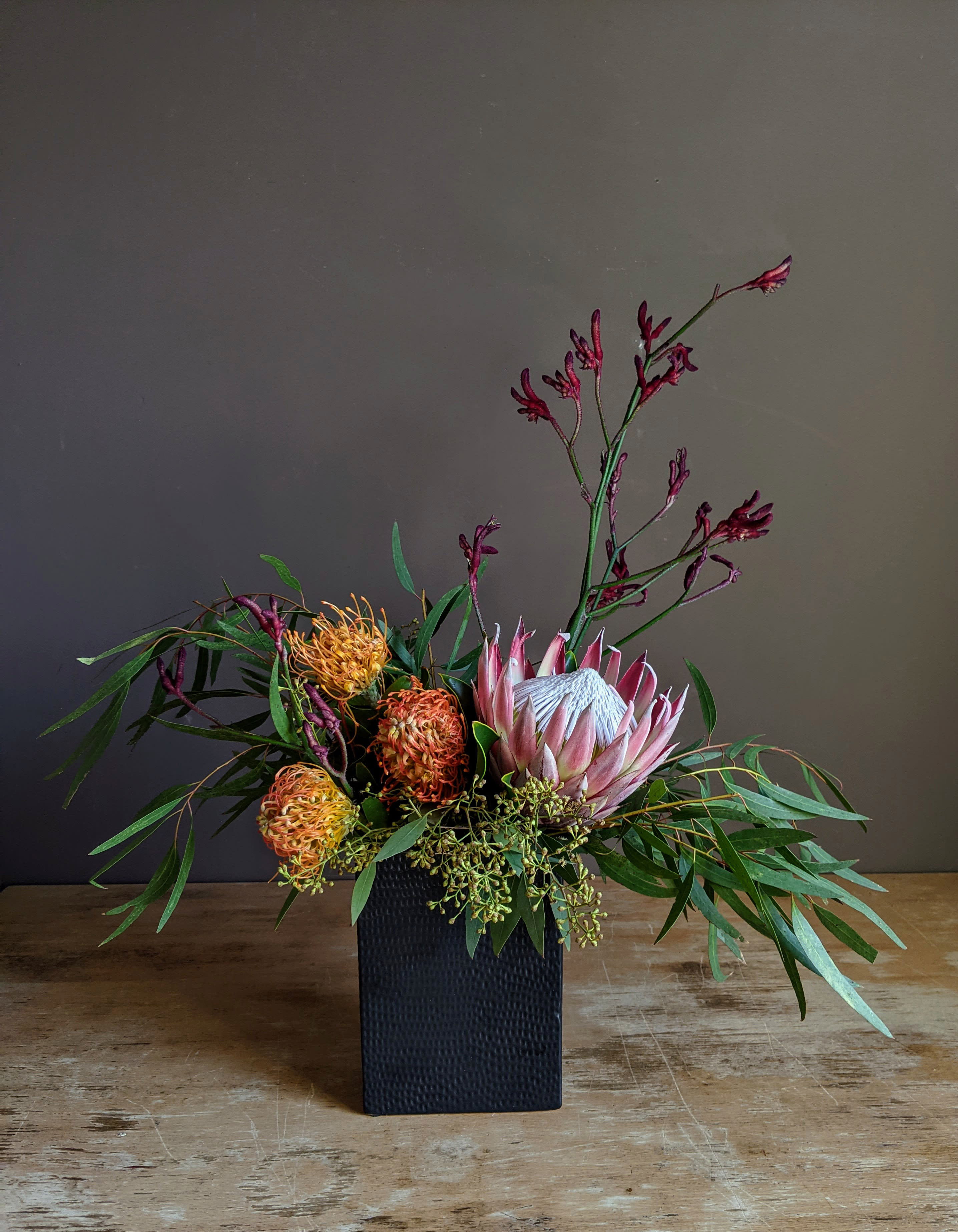 Arrangement of pink protea and orange pincushion blooms in a black vase