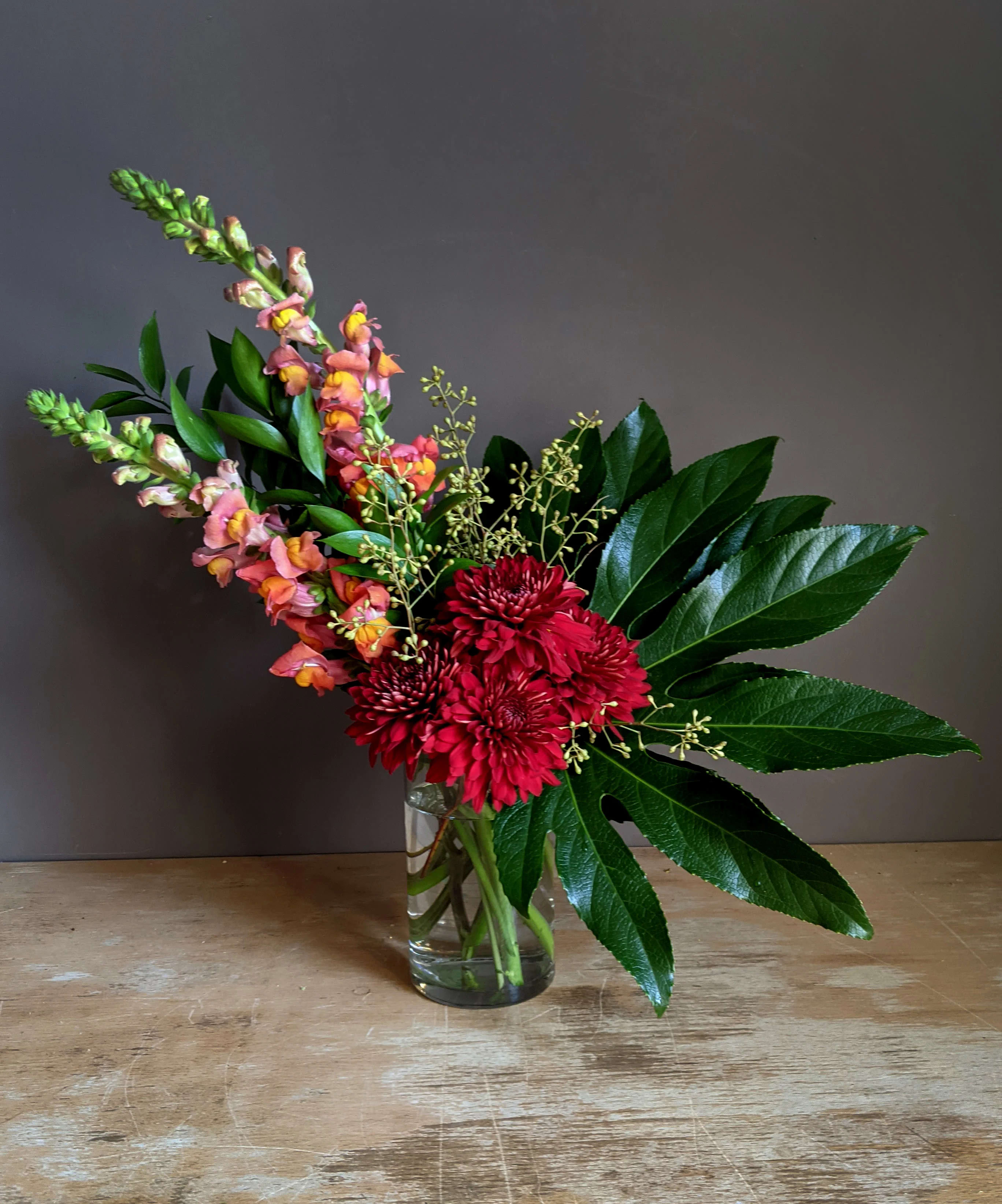 Red chrysanthemums and pink snapdragons in a clear glass vase