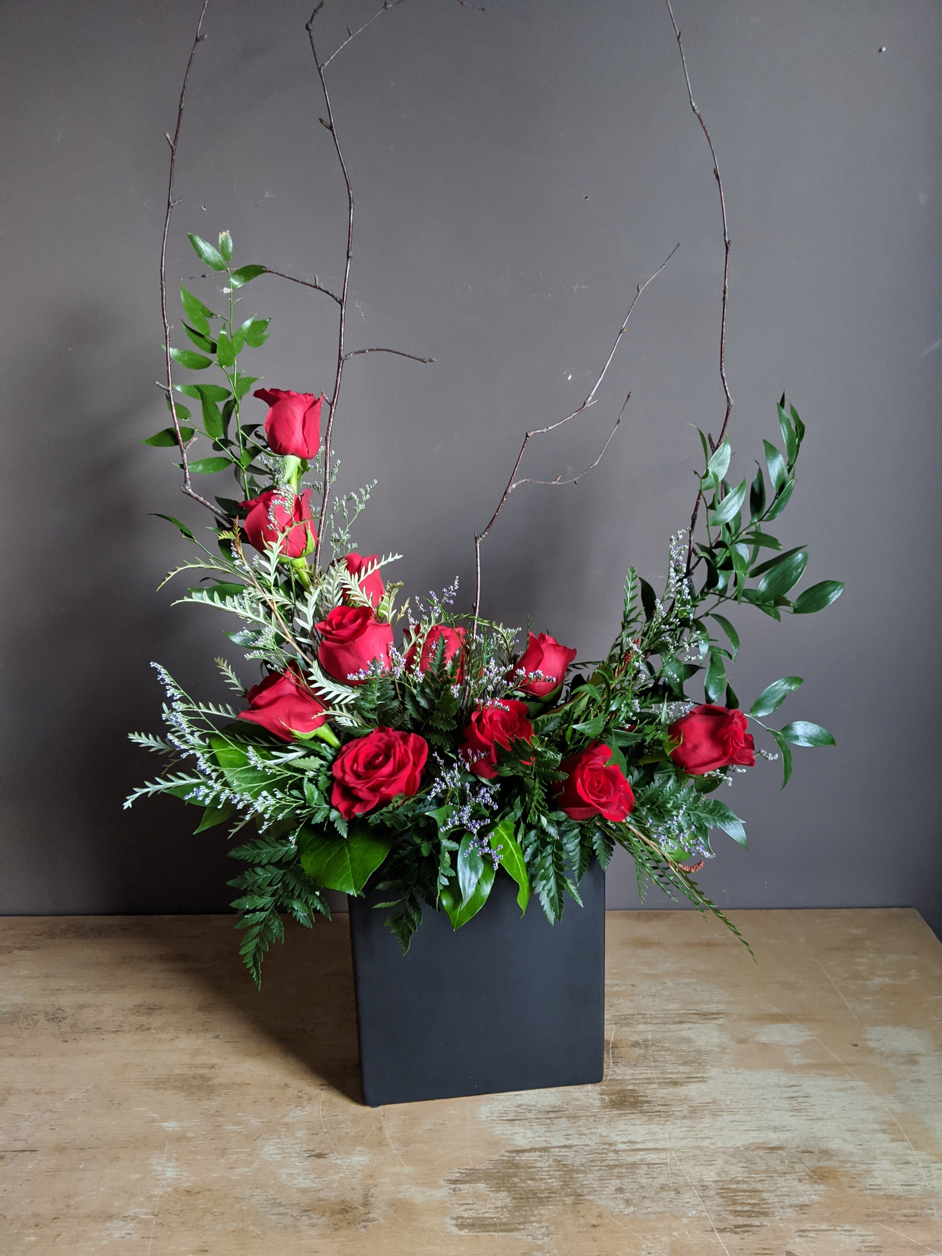 Red roses arranged in a tall black vase with branches and greenery