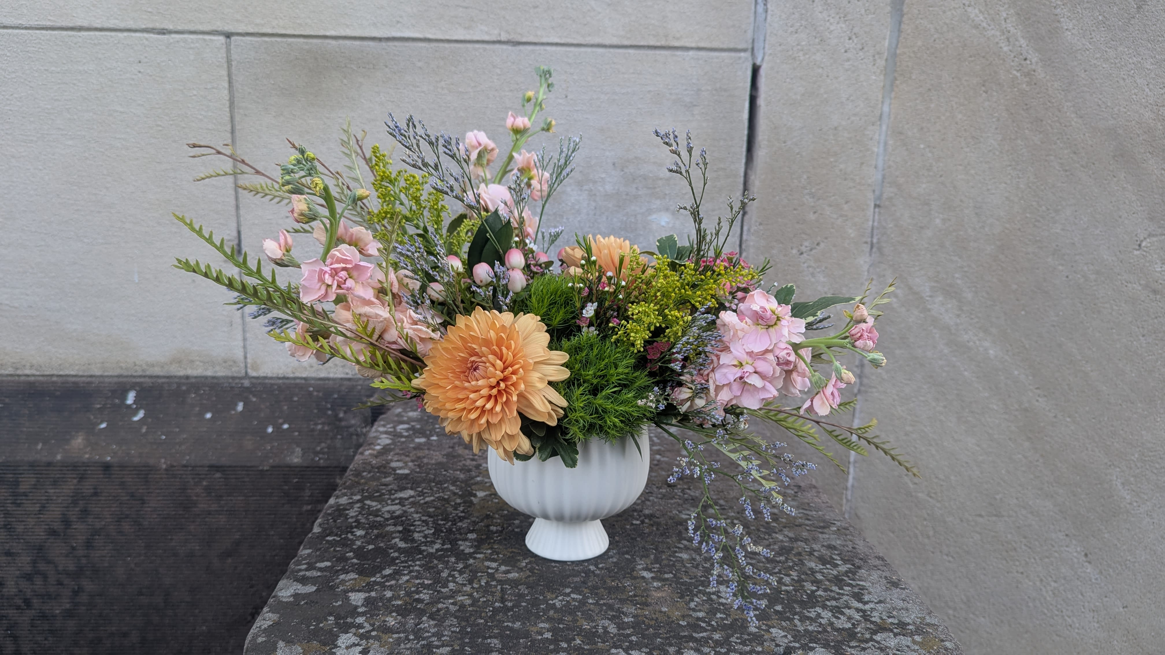 Pastel floral arrangement in a white pedestal vase with peach and pink blooms