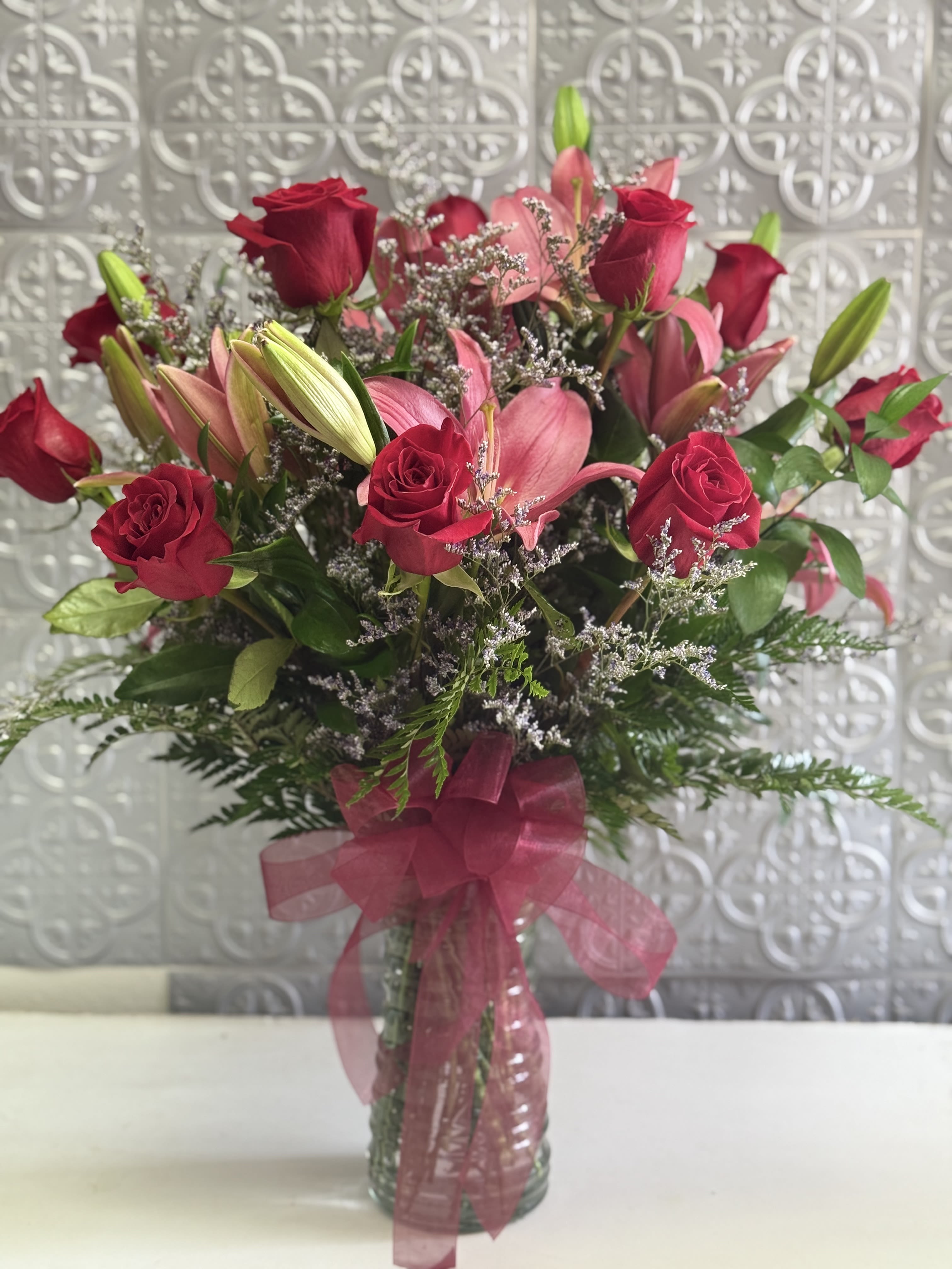 Bouquet of red roses and pink lilies in a clear glass vase with a pink ribbon
