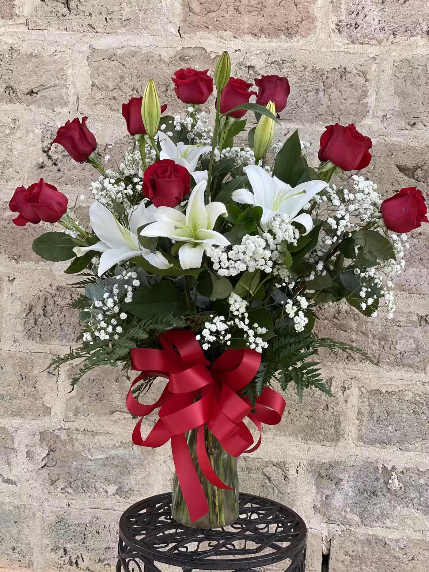 Red roses and white lilies in a glass vase with a red ribbon