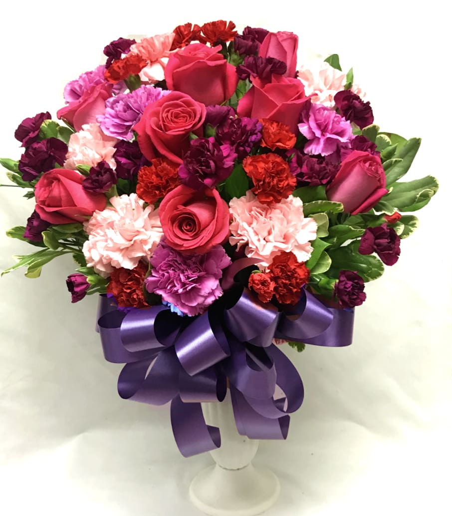Bouquet of pink roses and carnations in a white vase with a purple ribbon