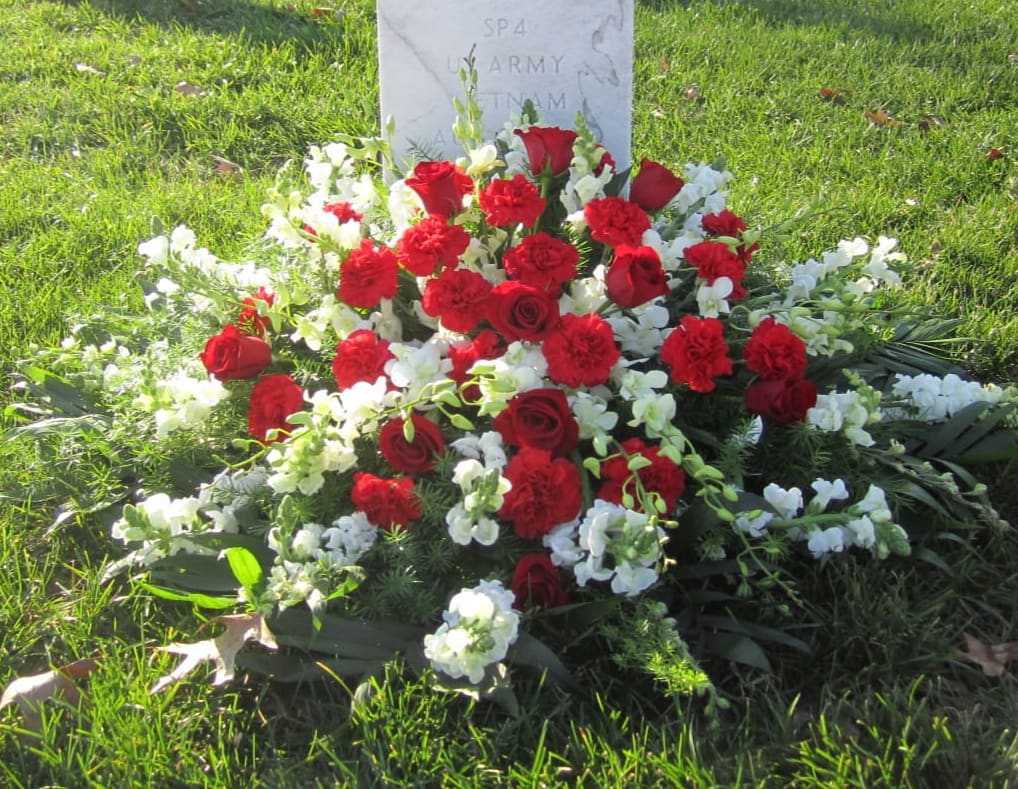 Red roses and carnations arranged at a gravestone with white flowers