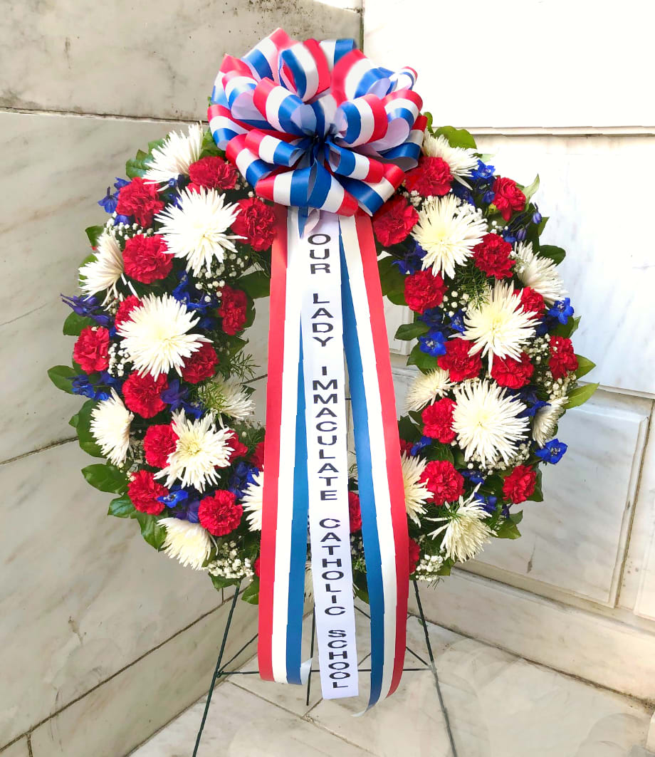 Standing floral wreath with red, white, and blue flowers and a memorial ribbon