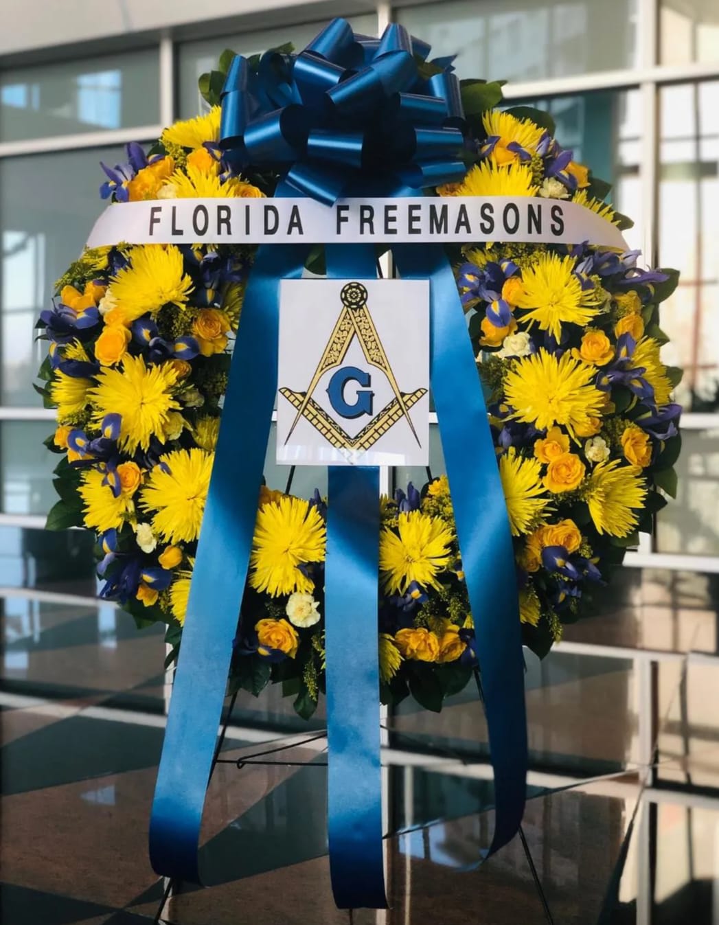 Large floral wreath with yellow and blue flowers and a blue ribbon bow