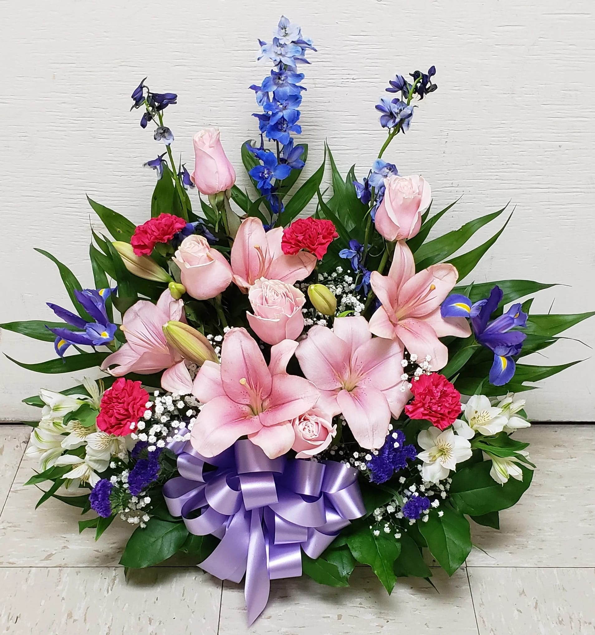 Pink lilies and roses with blue flowers in a lavender ribboned arrangement