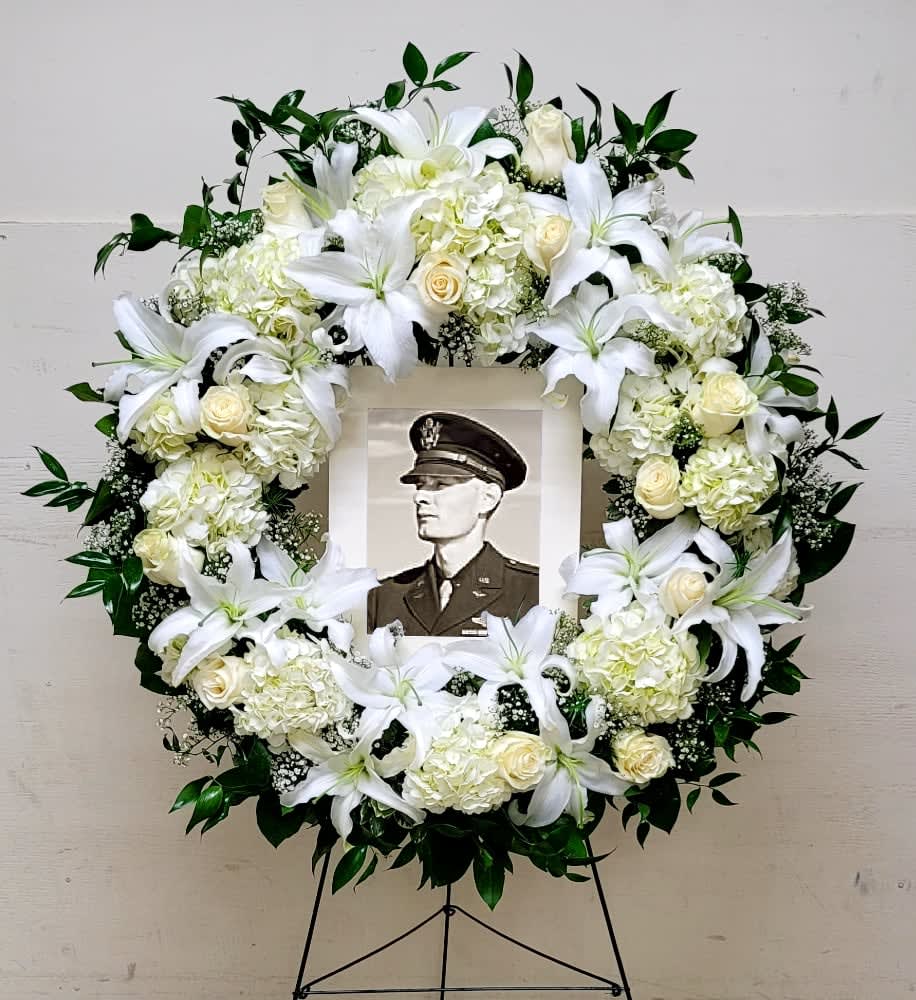 White floral funeral wreath with a framed portrait in the center