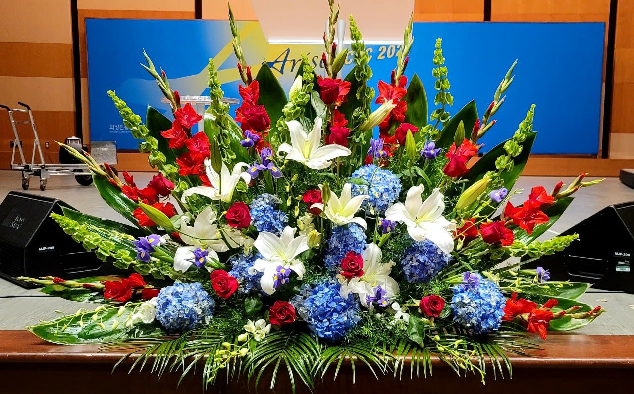 Large red, white, and blue stage floral spray with lilies, roses, gladiolus, and hydrangeas.