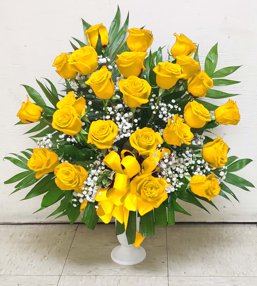 Yellow roses arranged in a white pedestal vase with baby's breath