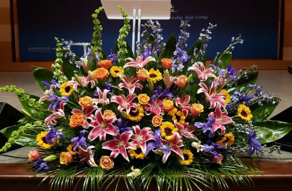 Large altar arrangement of pink lilies, orange roses, yellow sunflowers, and blue delphinium