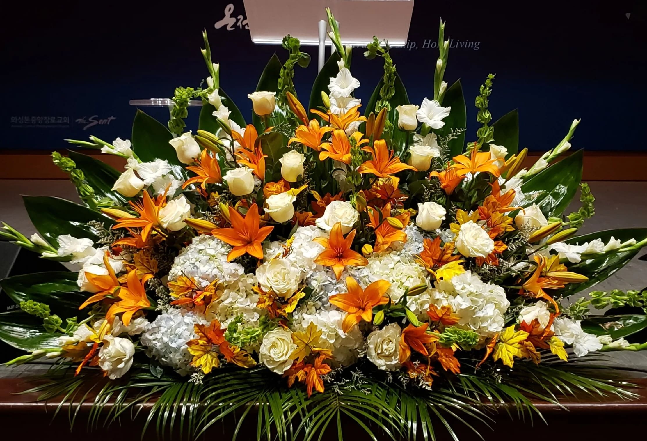 Large altar-style arrangement of orange lilies and white roses with hydrangeas in a low horizontal design
