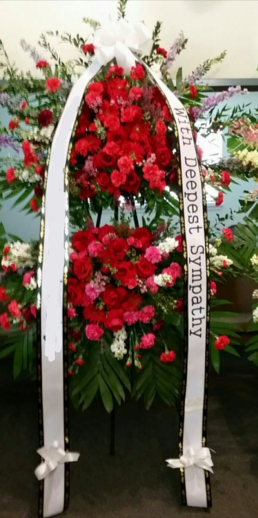 Standing sympathy wreath of red and pink flowers with white ribbon