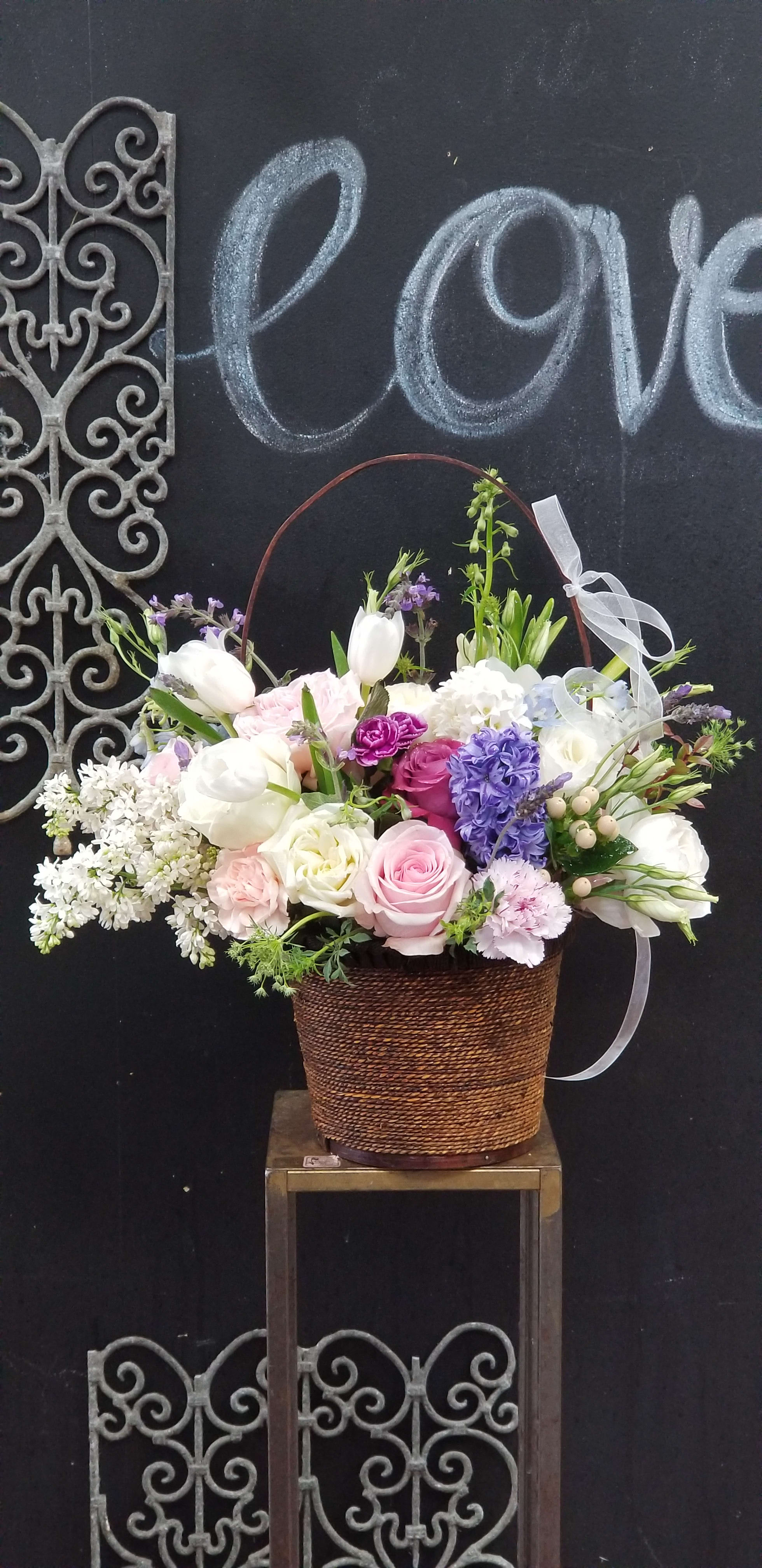 Basket arrangement of pink, white, and purple flowers with a ribbon bow