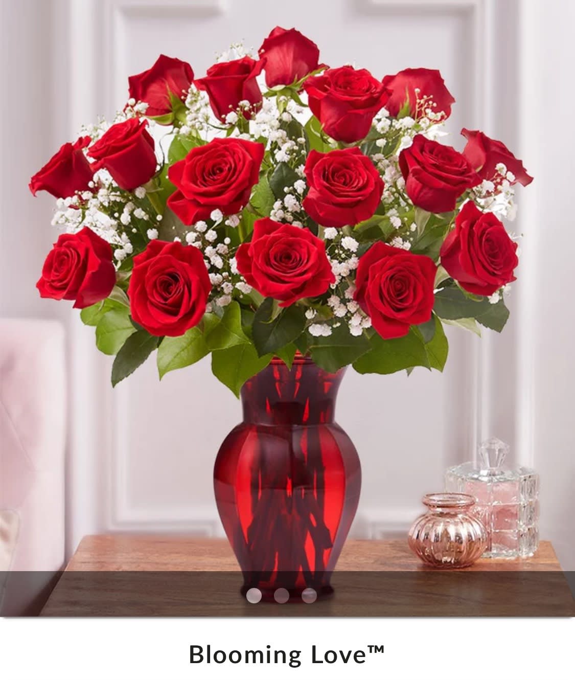 Red roses arranged in a red glass vase with white baby's breath