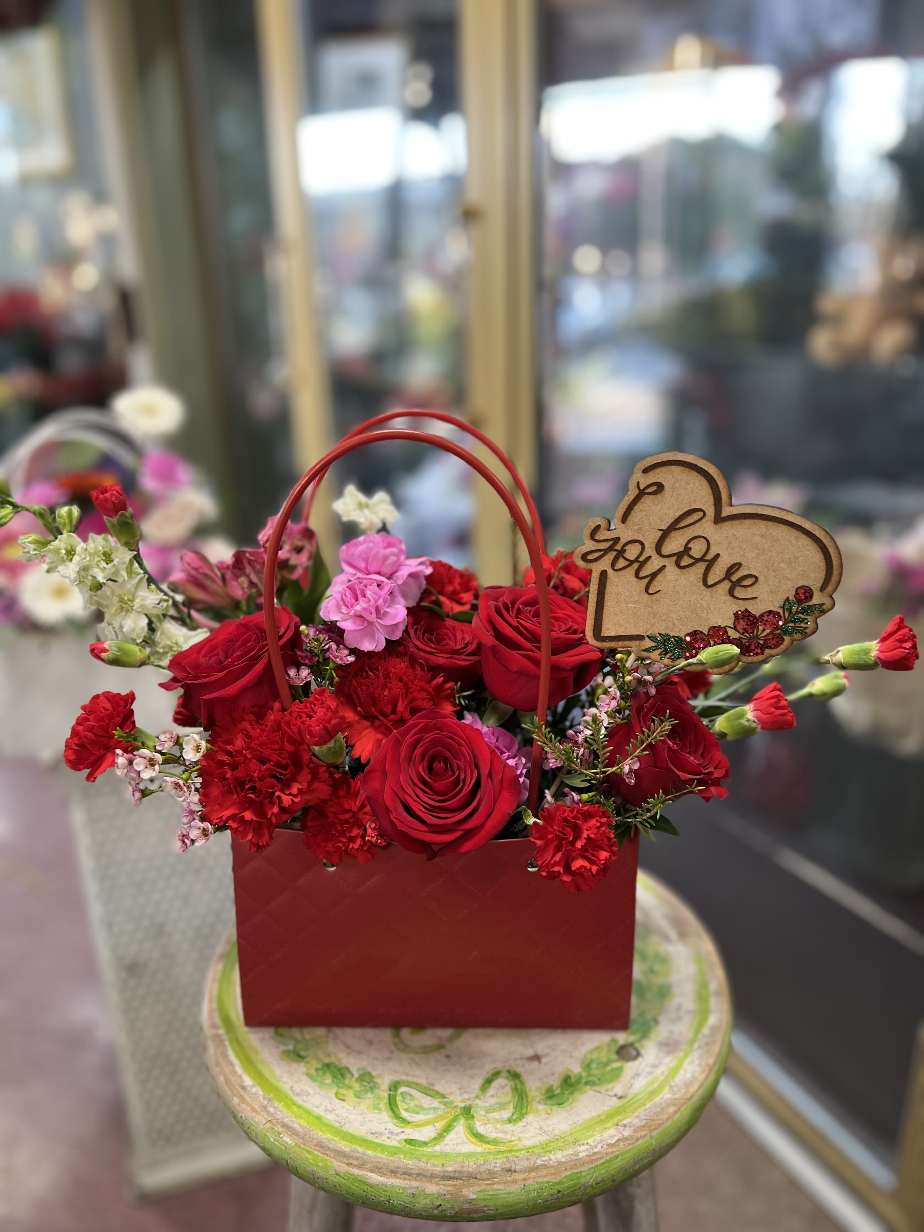 Red rose and carnation arrangement in a red handled gift box with a love sign
