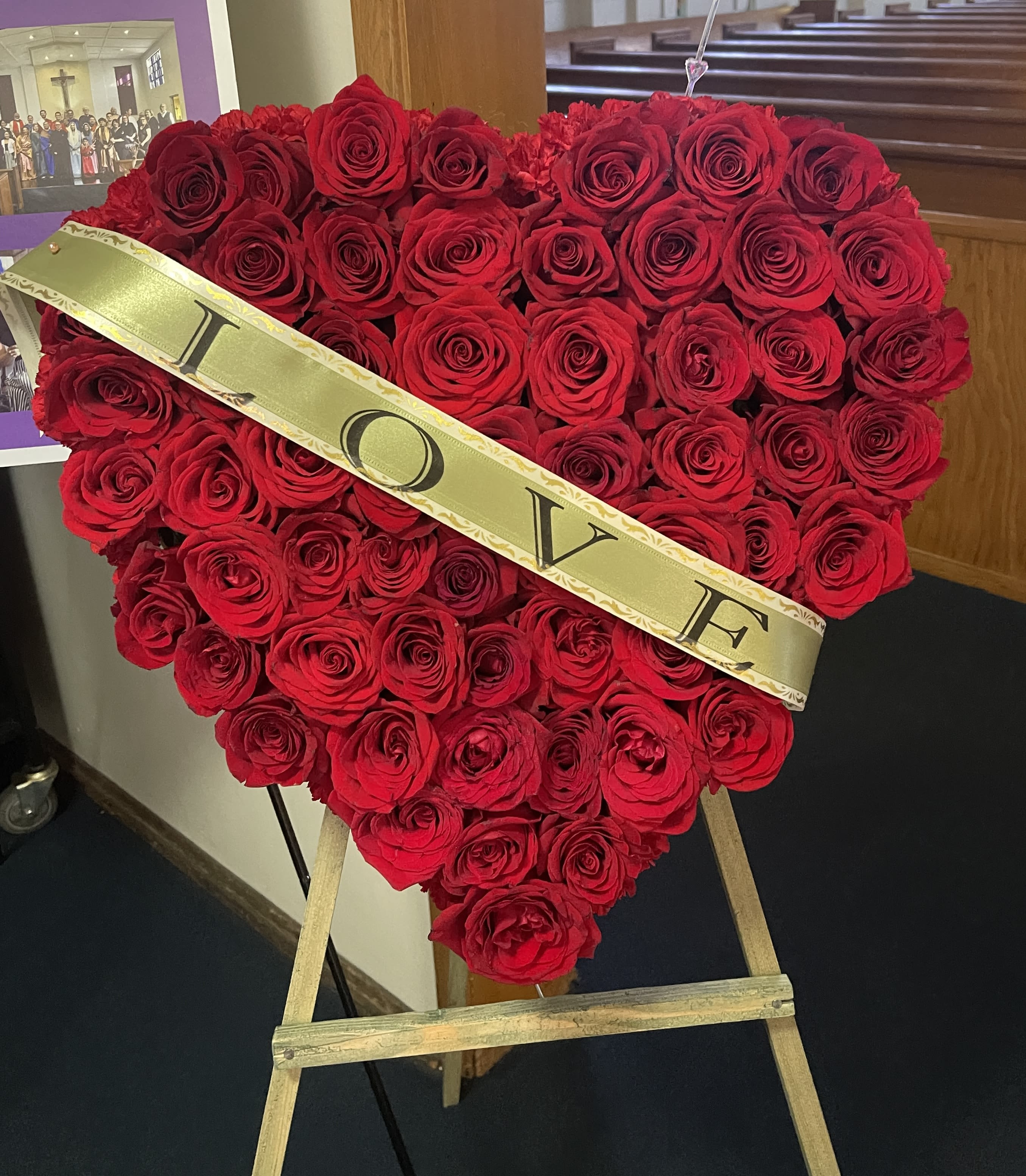 Heart-shaped red rose arrangement on an easel with a gold LOVE sash