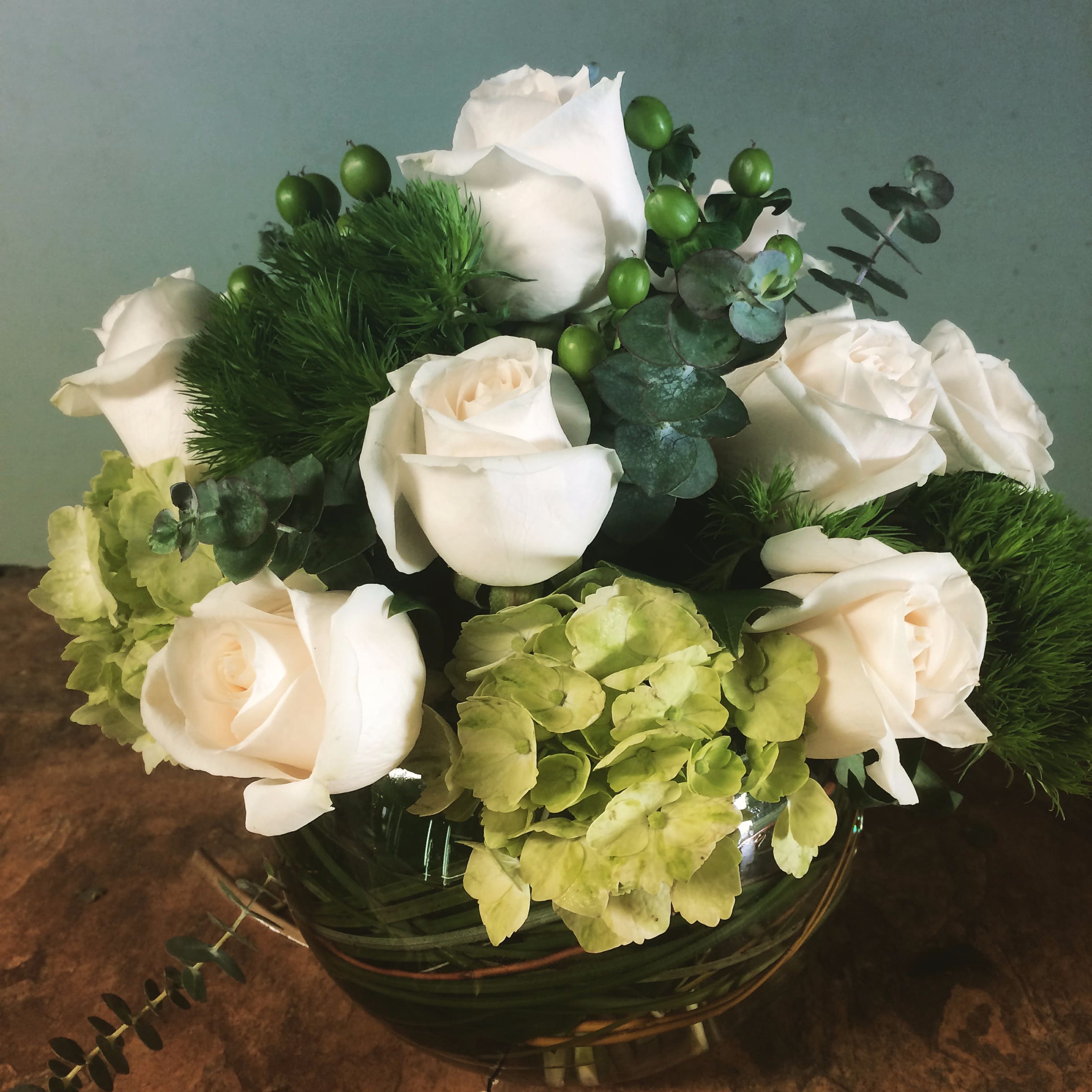 White roses and green hydrangeas in a glass bowl vase