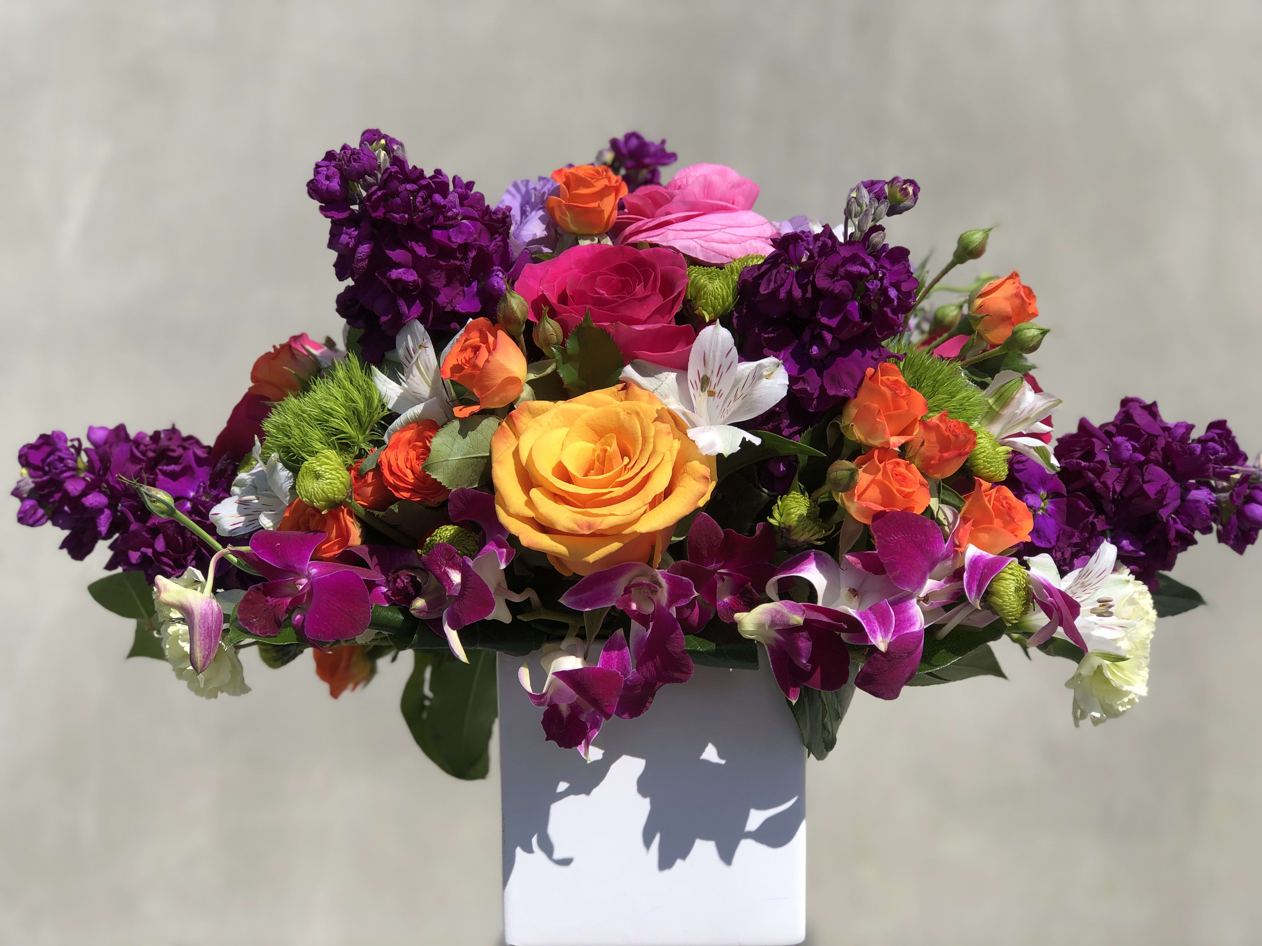 Bright mixed bouquet with roses, orchids, and purple blooms in a white vase