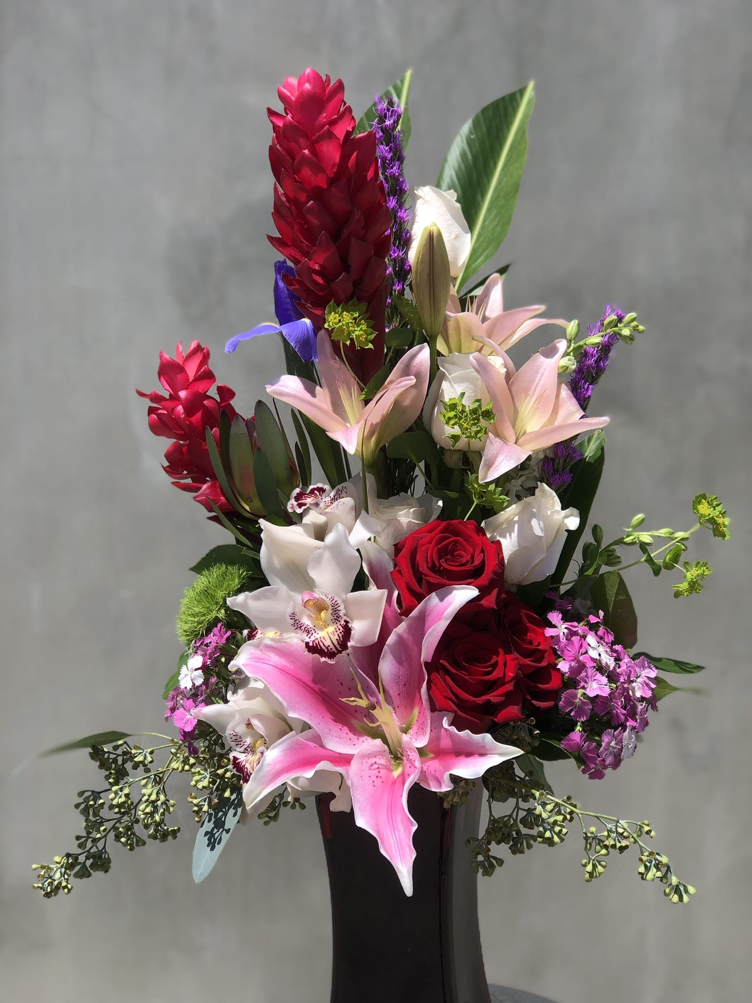 Tall bouquet of red roses, pink lilies, and orchids in a black vase