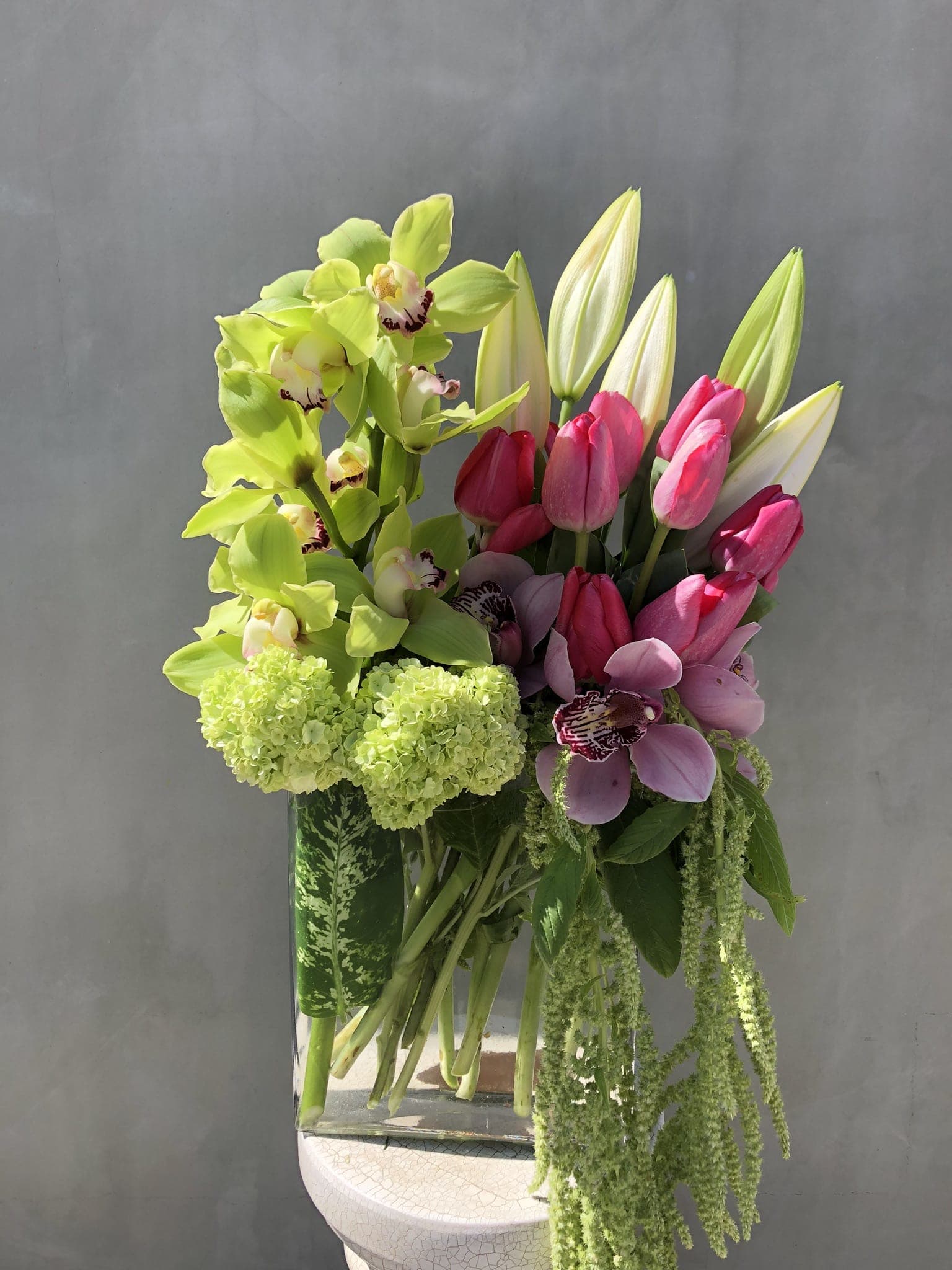Arrangement of green orchids, pink tulips, and lilies in a glass vase