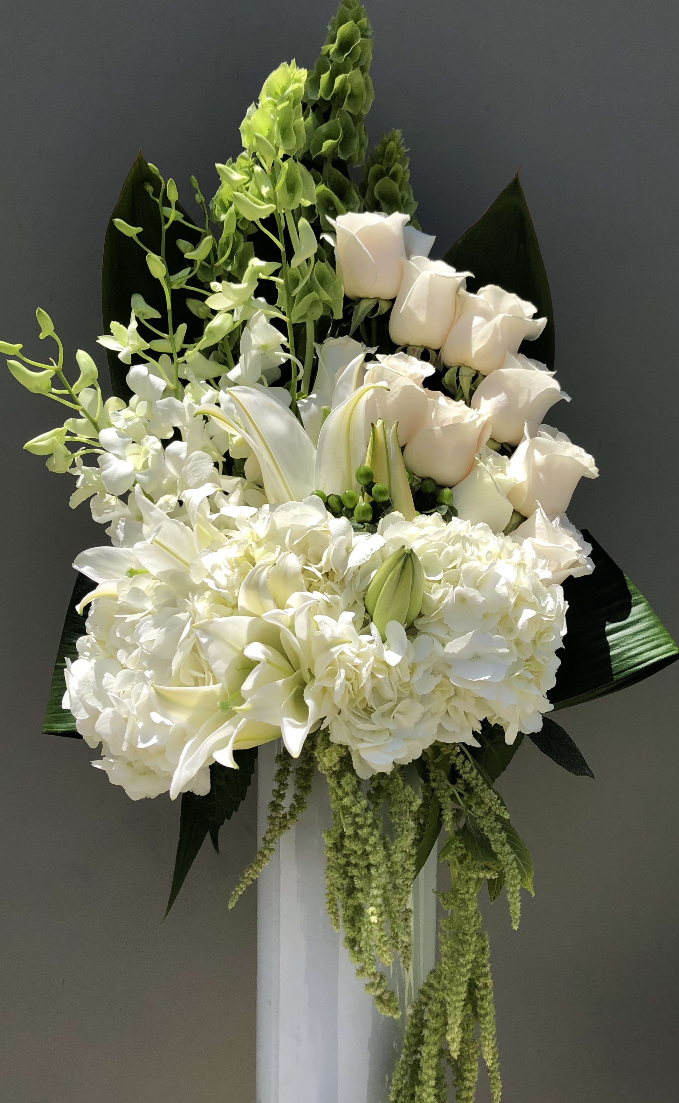 White floral arrangement with roses, lilies, and orchids on a pedestal