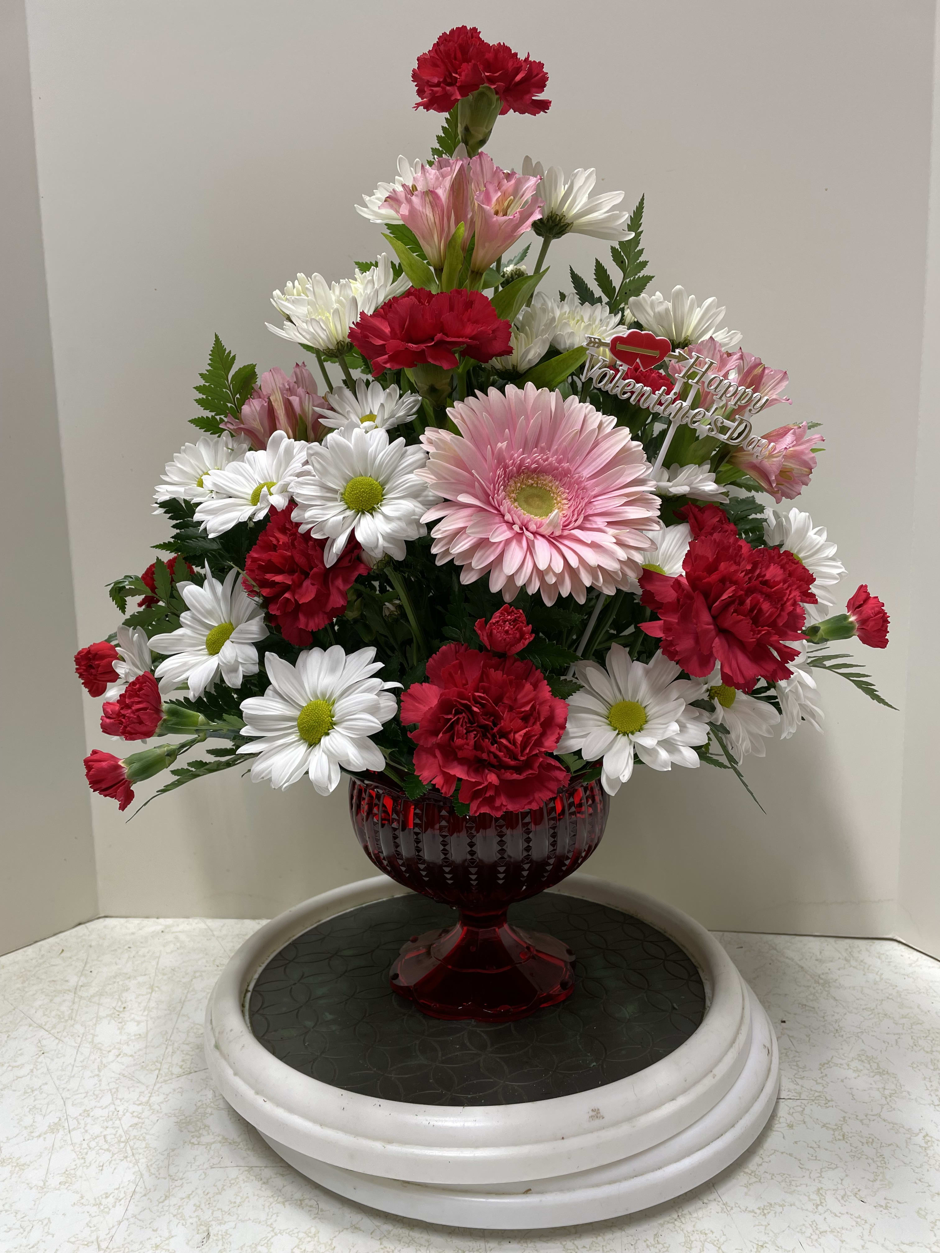 Peak of My Love Bouquet - This unique design is filled with an array of pink, red, and white blossoms and various greenery.  Carnations, both large and miniature, cushion pom pons, daisies, and alstroemeria lilies combine for a beautiful presentation.  The pedestal ruby red contained is the perfect presentation piece for these lovely blooms that speak of love and romance.  We only have a limited number of vases (8), so order early to ensure availability.  