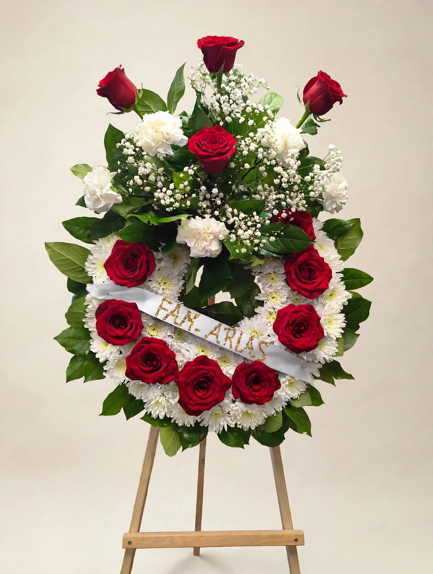 Red roses and white flowers arranged on a standing easel with a ribbon