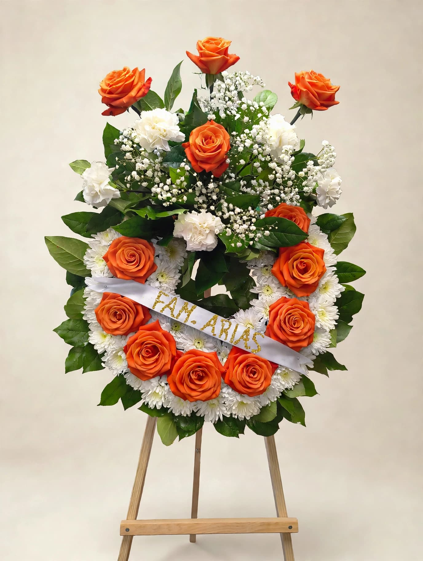 Orange roses and white flowers arranged on a standing easel wreath