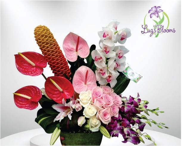 Tropical floral arrangement with red anthuriums, orchids, roses, and a pinecone ginger bloom