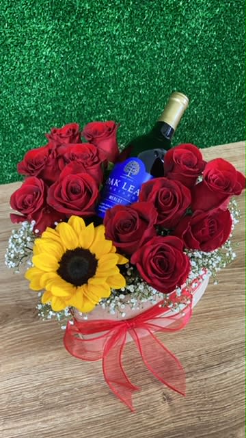 Red roses and a sunflower arranged around a wine bottle in a gift box
