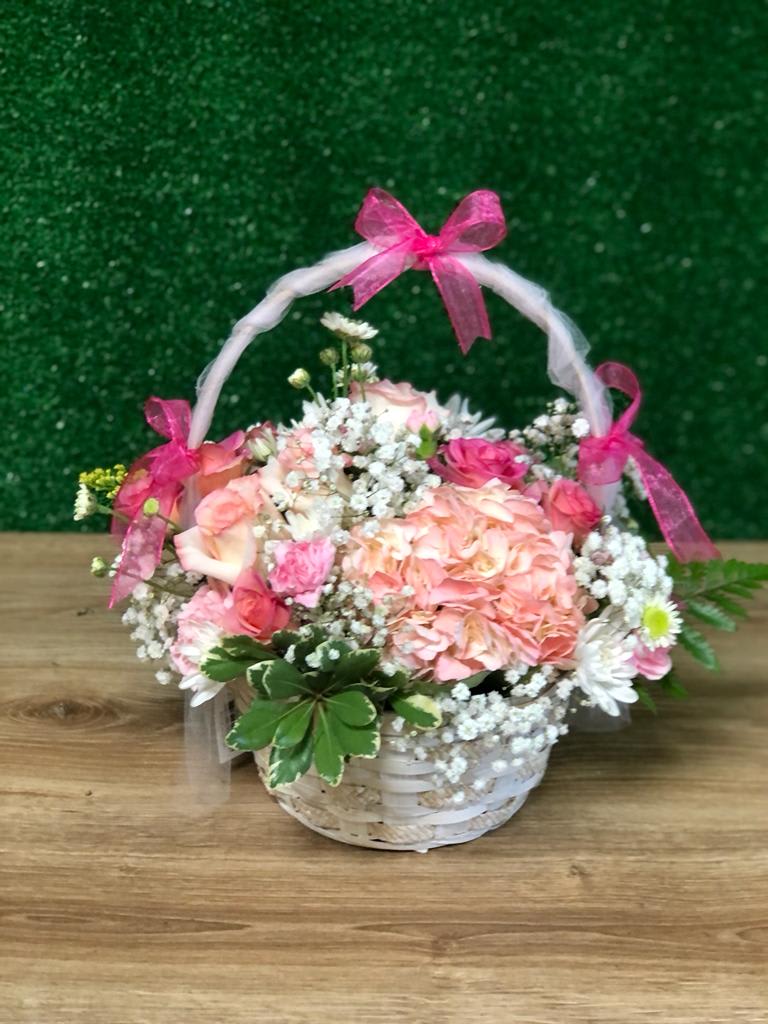 White basket of pink and white flowers with baby’s breath and pink bows on the handle