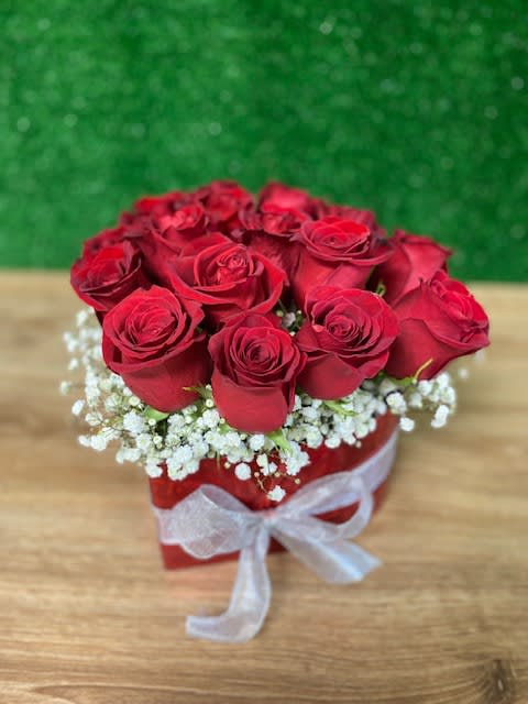 Short arrangement of red roses in a red box with white accent flowers and a white ribbon bow