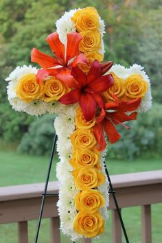 Standing cross-shaped floral spray with yellow roses, white blooms, and orange lilies on an easel