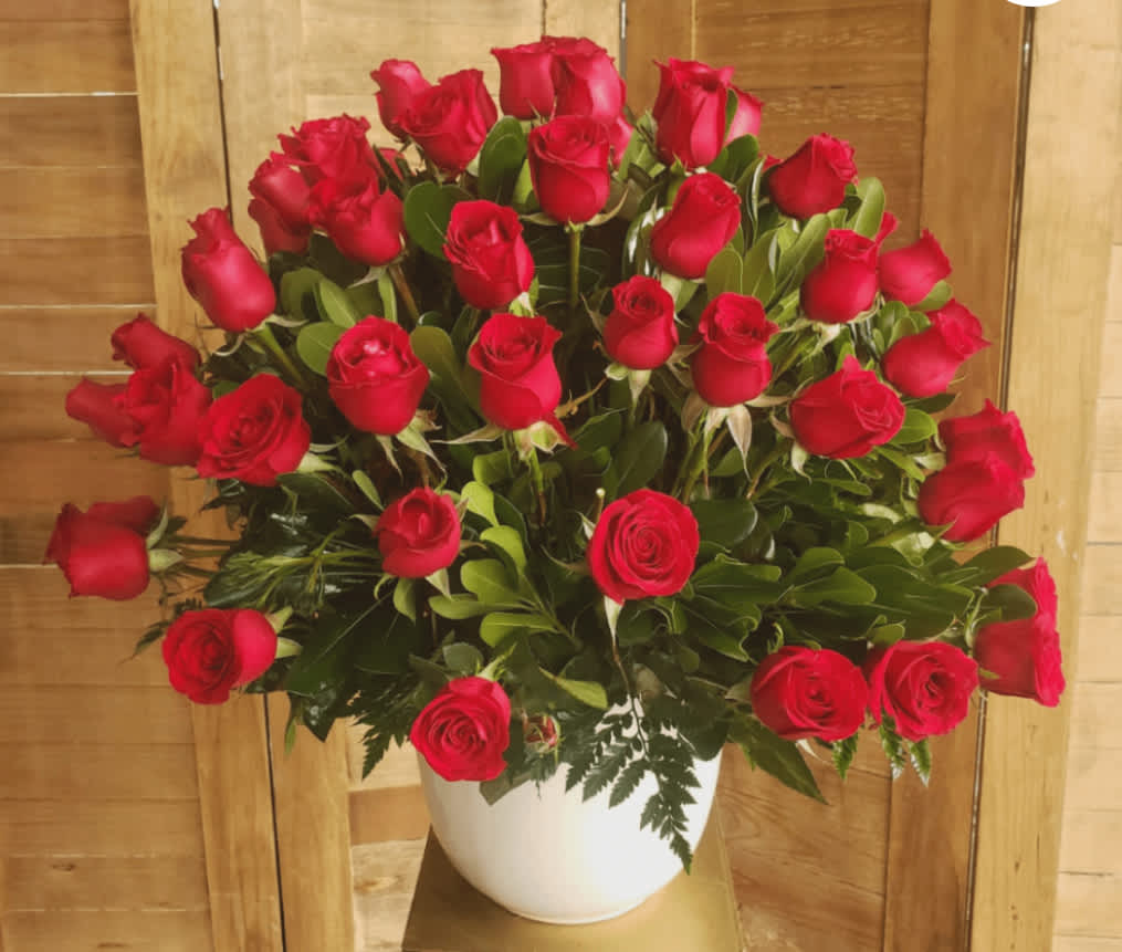 Large arrangement of red roses in a white ceramic pot against a wood background