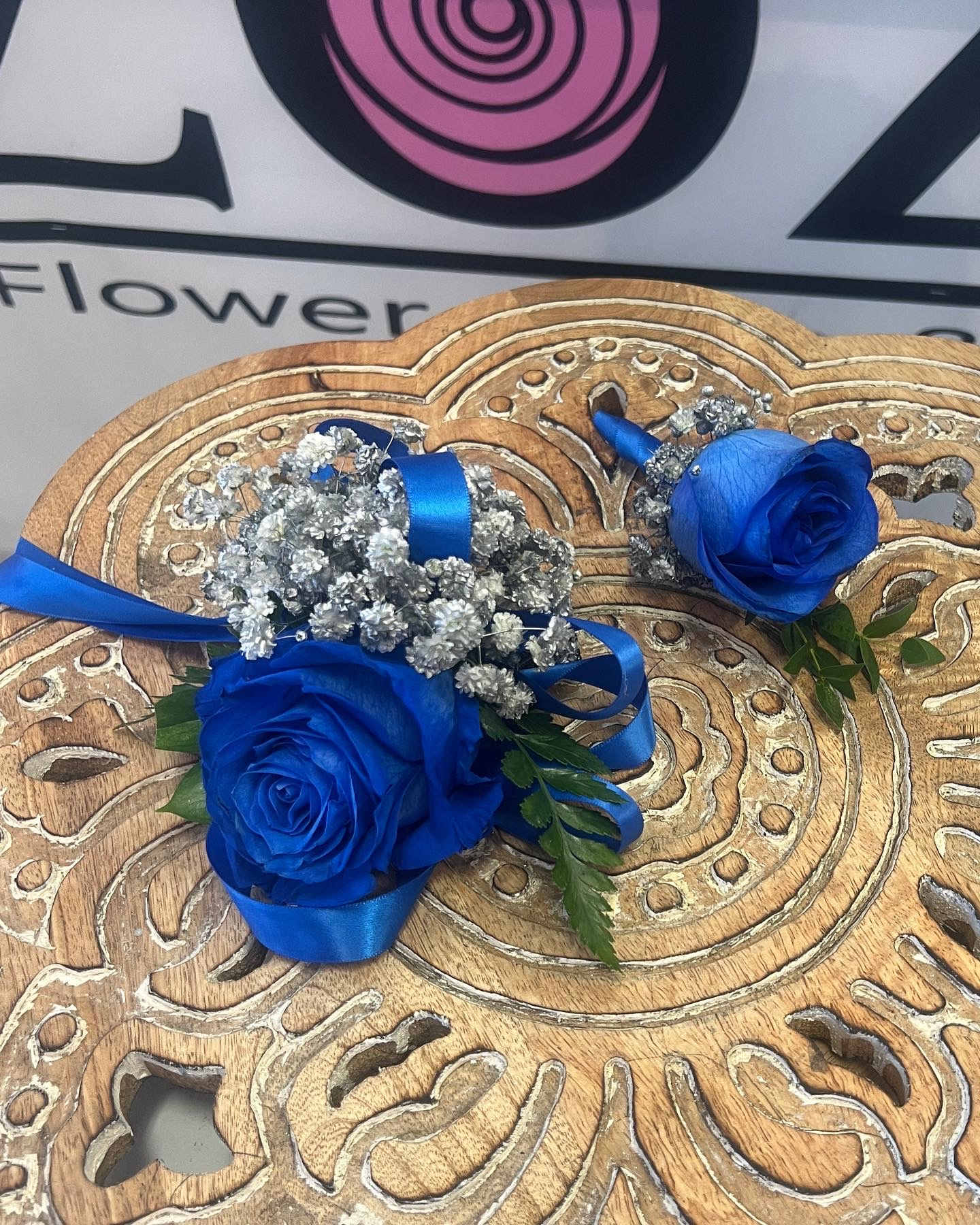 Two blue rose boutonnieres with silver baby's breath and ribbon