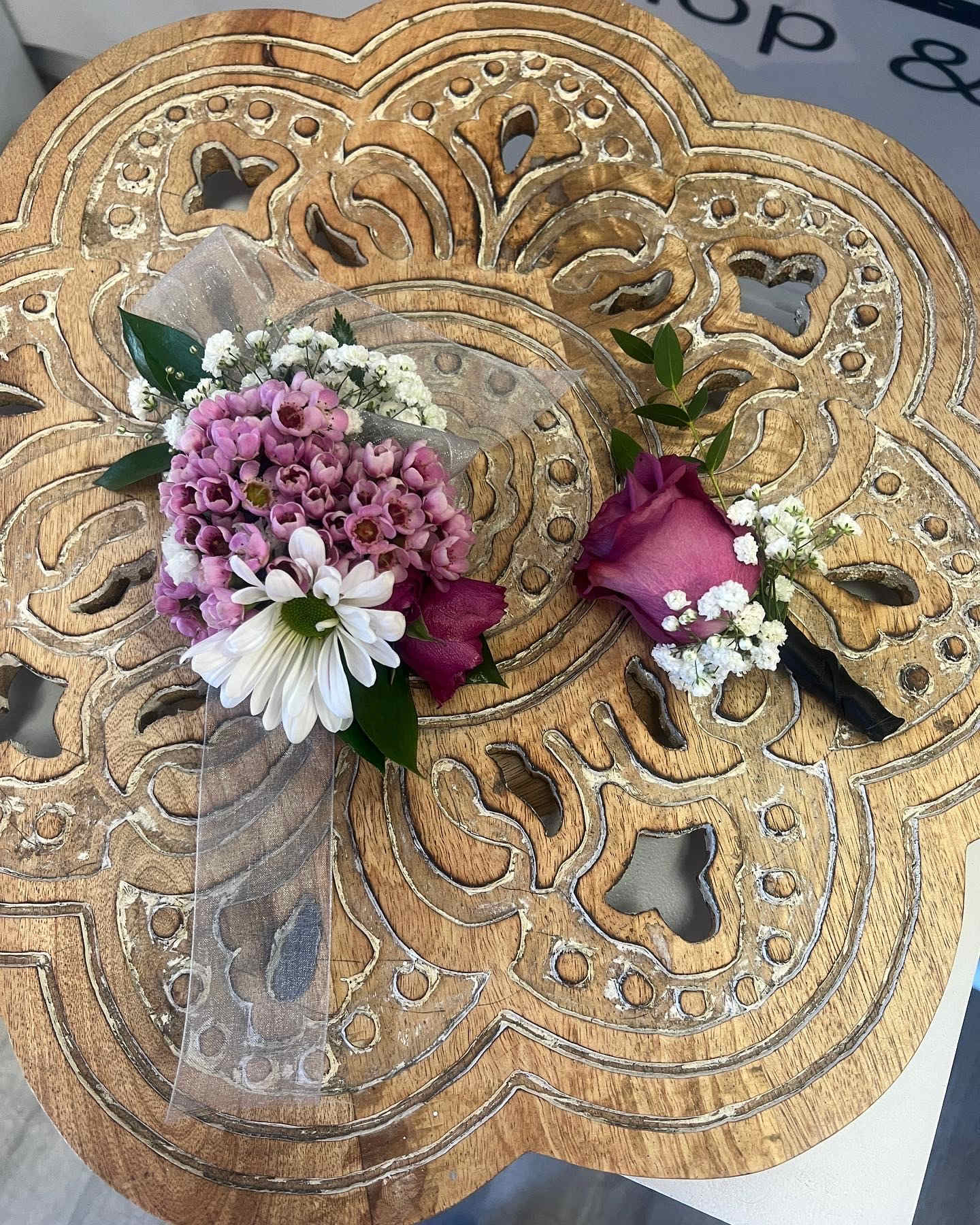 Pink and white corsage and boutonniere set on a carved wooden table