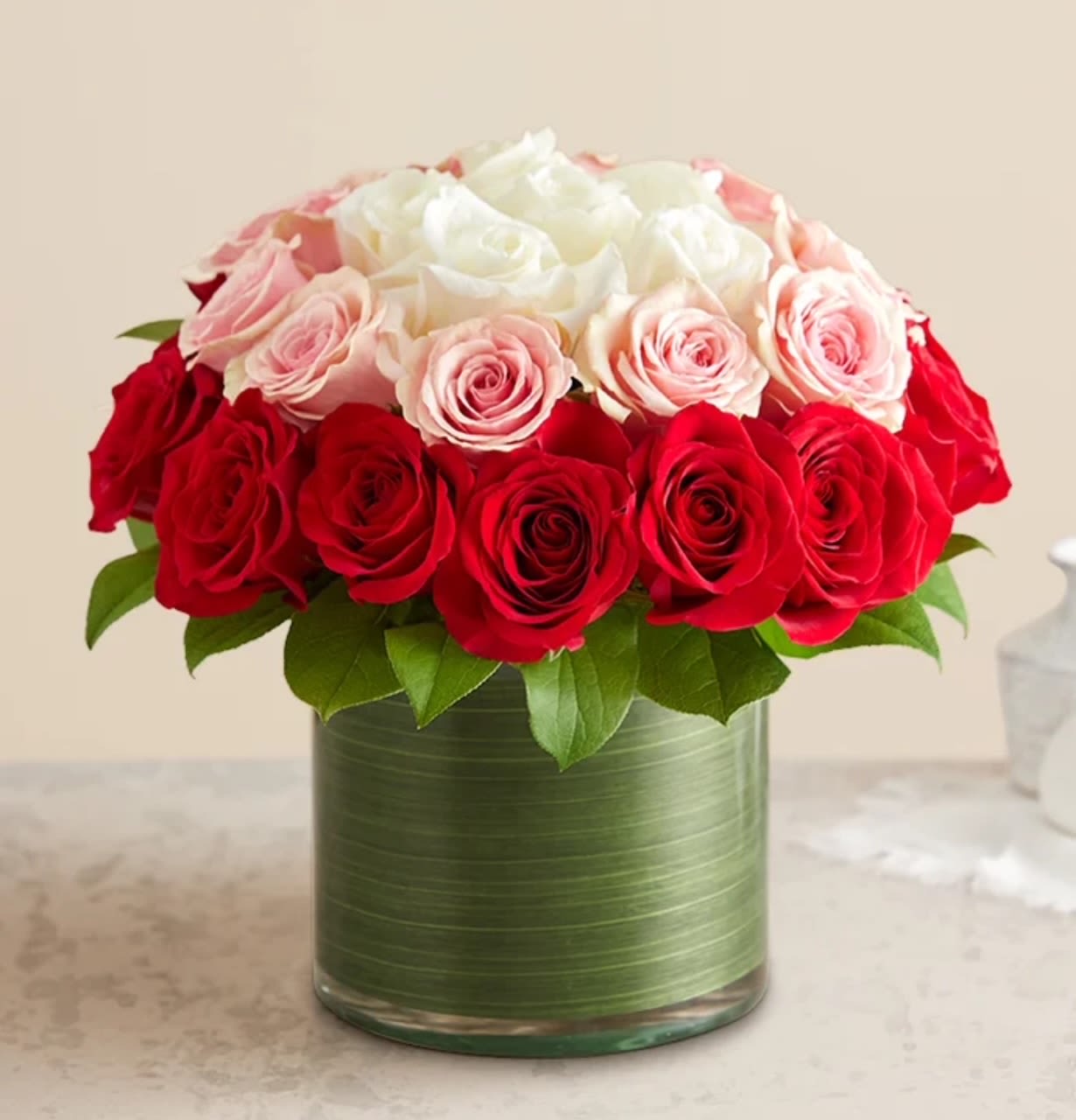 Round arrangement of red, pink, and white roses in a clear glass cylinder vase