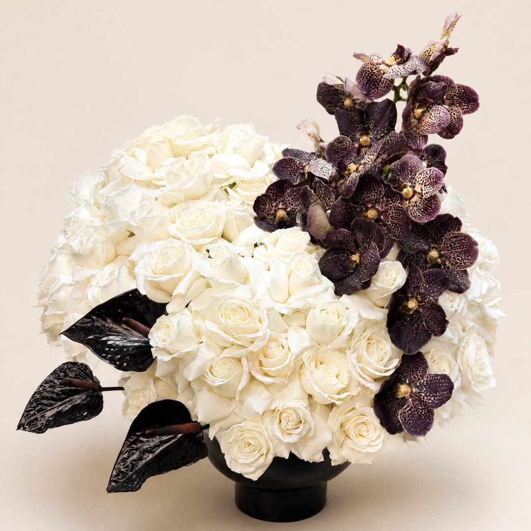 White rose arrangement with dark purple orchids in a black vase