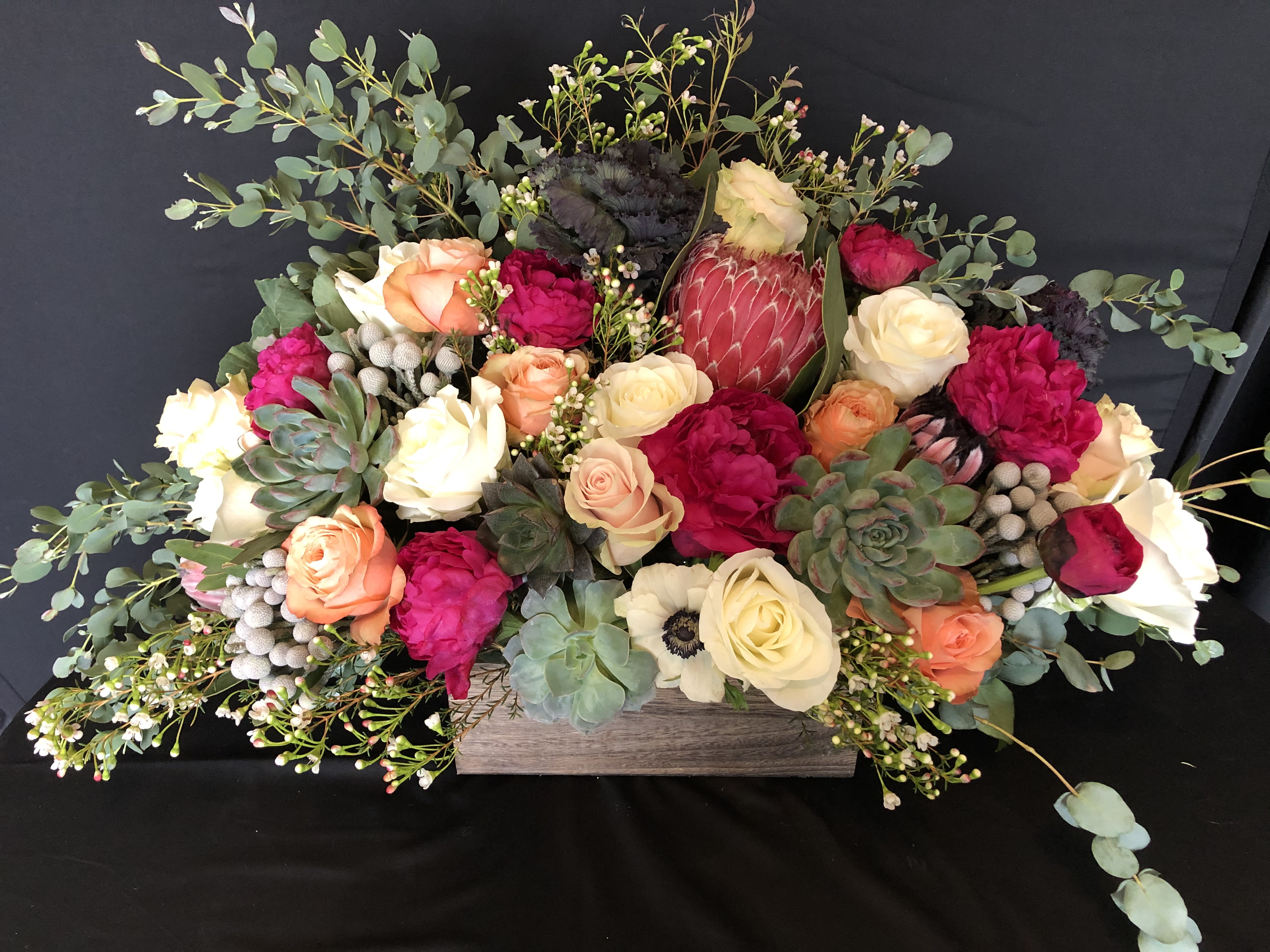 Low floral arrangement with roses, protea, and succulents in a wooden box
