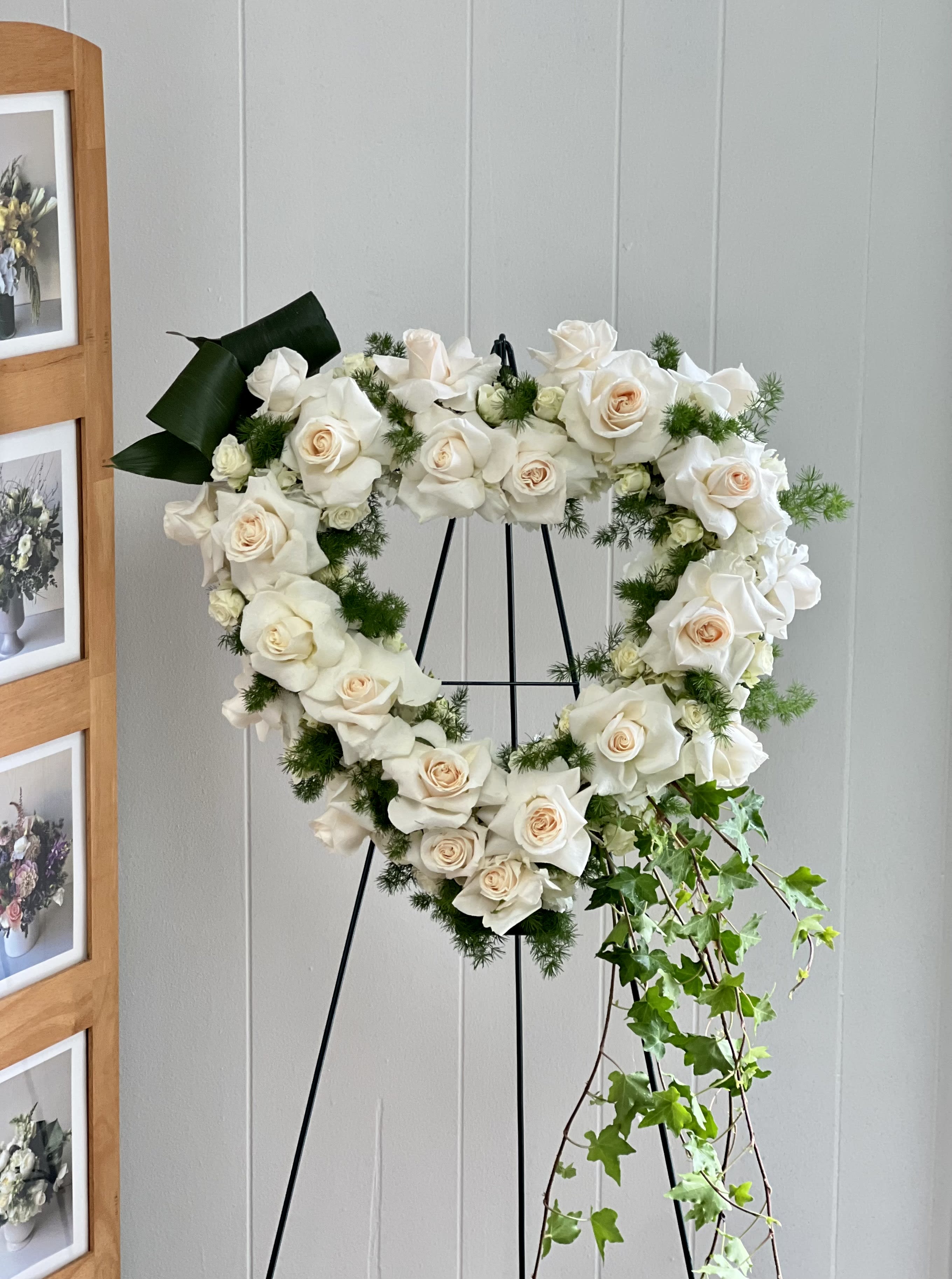 SYM02 - Love in our Hearts  - The Love in our Hearts floral wreath is an excellent choice for a heartfelt tribute or as a symbol of love and remembrance. This beautiful heart-shaped wreath is carefully crafted with a mixture of timeless white blooms and textured greenery that make it an elegant and serence display that is sure to be cherished. Hung on a sturdy easel, this wreath is a beautiful and poignant display that is perfect for commemorating a loved one's life or celebrating a special occasion. 