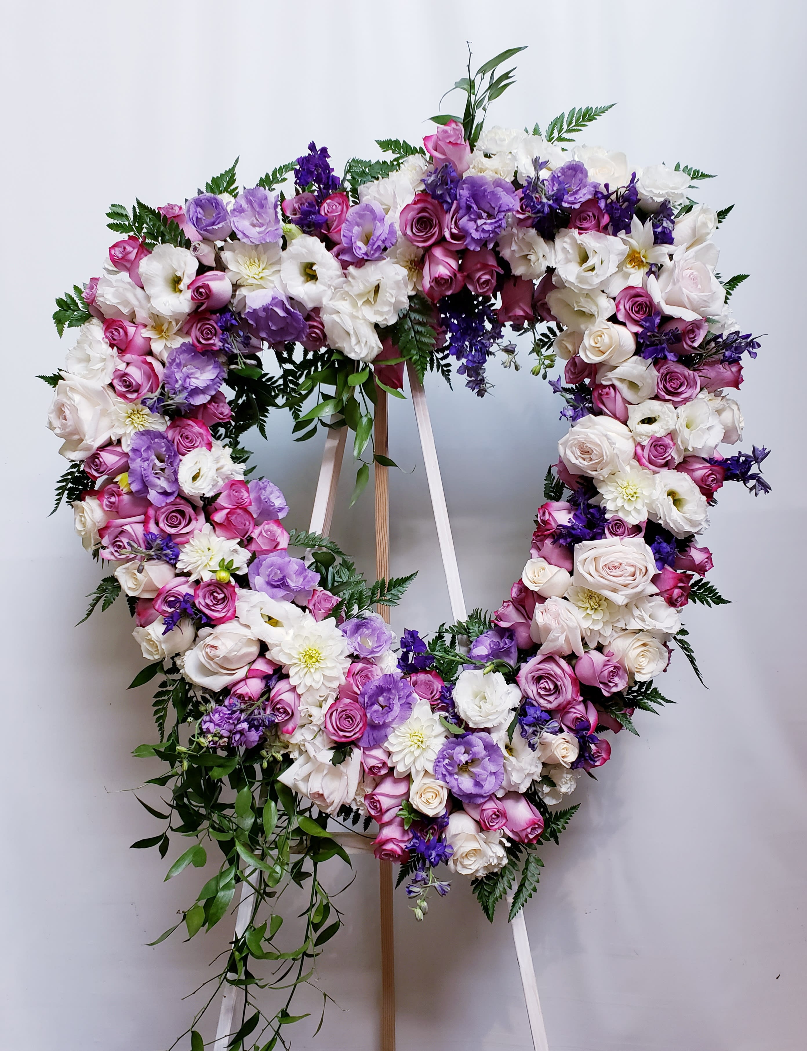 Heart-shaped floral wreath with pink, white, and purple blooms on a stand