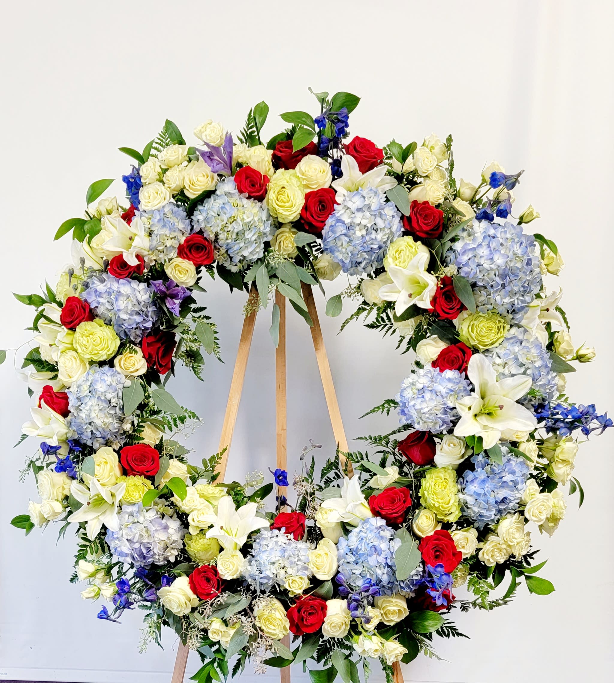Large floral wreath of red, white, blue, and pale yellow flowers on a wooden stand
